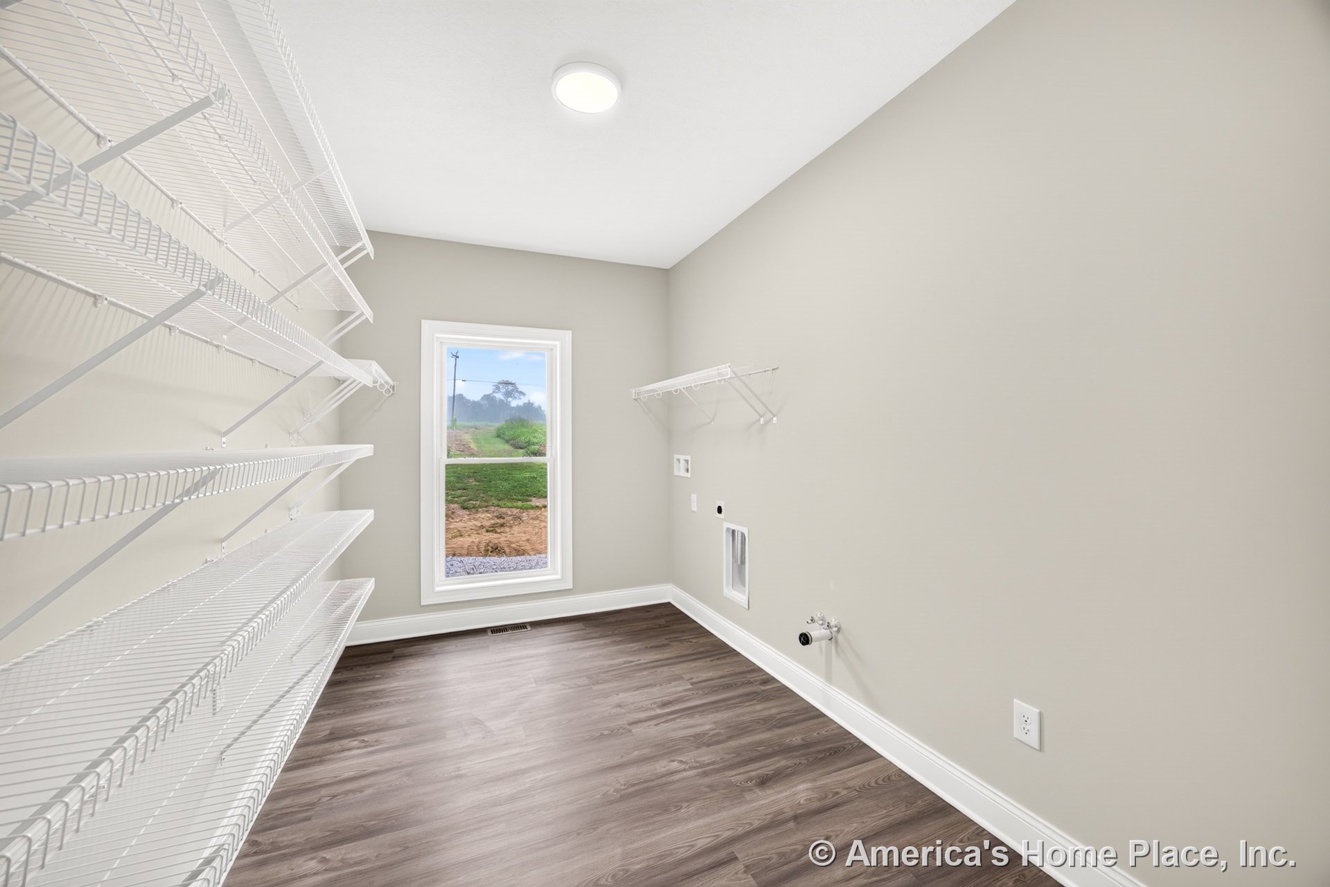 Utility pantry with wall-mounted wire shelving, large window with trim, laundry hookups, vinyl plank flooring, neutral painted walls, baseboard, and flush ceiling light.