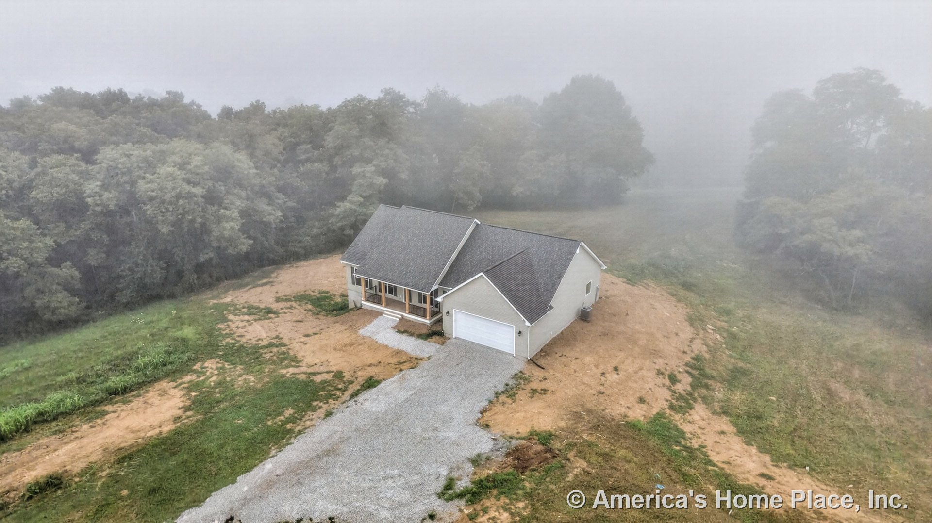 Single-story home with covered front porch, attached two-car garage, gabled roof, horizontal exterior siding, and gravel driveway in a rural setting.