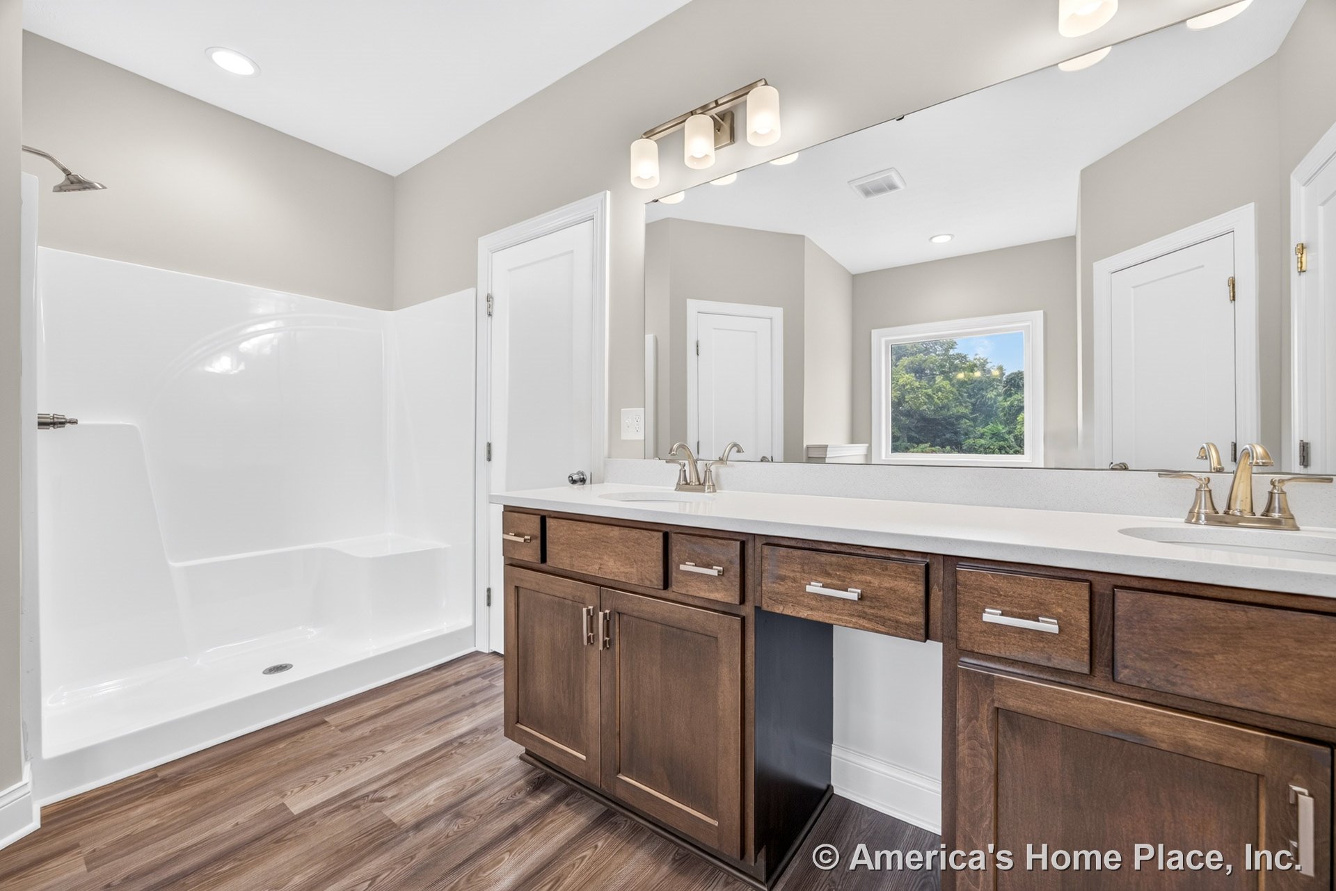 Double-sink vanity with wood cabinetry and stone countertop, large wall mirror above, walk-in shower with built-in seat and glass enclosure, recessed ceiling lights, window with