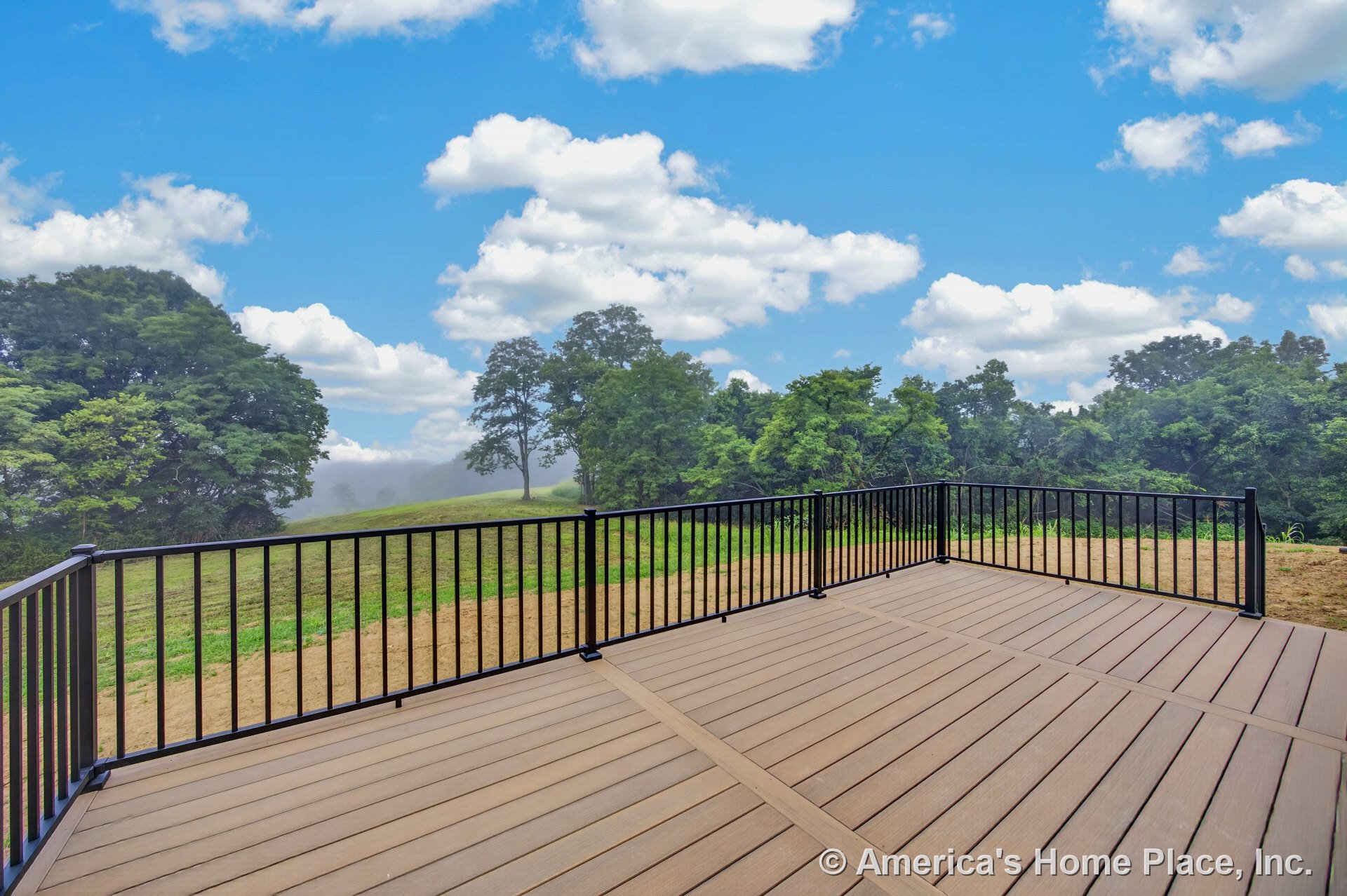 Composite deck with black metal railings on raised platform overlooking open grassy yard and landscaped exterior space