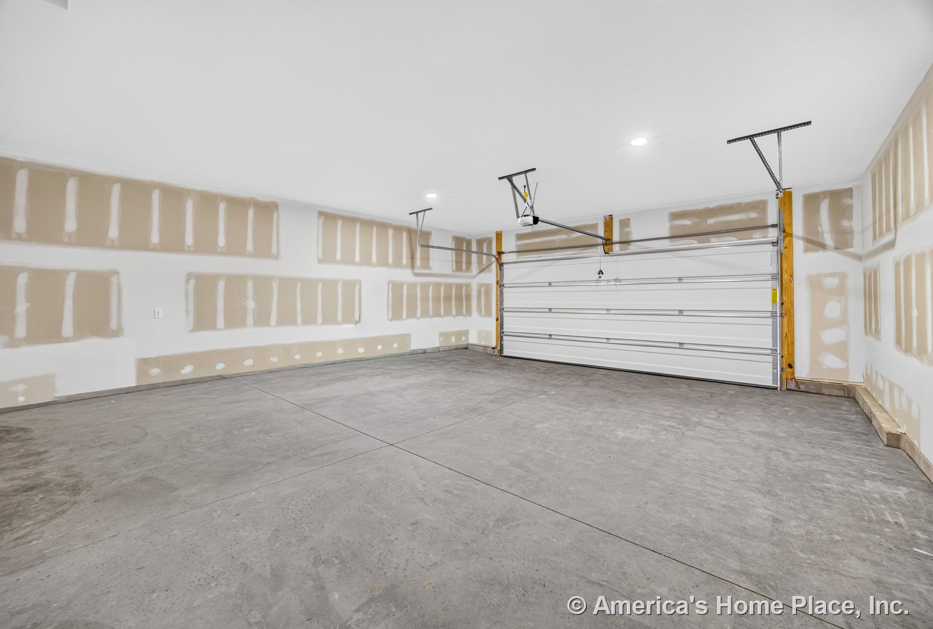 Unfinished garage with exposed drywall, concrete slab floor, double overhead doors equipped with automatic openers, recessed ceiling lights, and visible framing around entry.