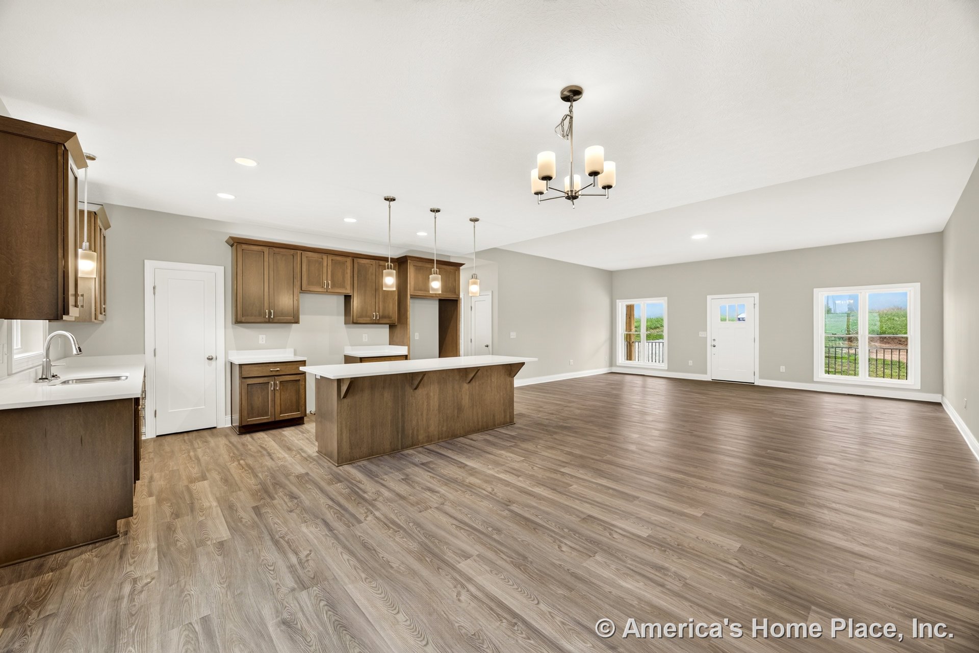 Wood kitchen cabinets and white solid surface countertops with pendant lights above the island, open to a spacious living area featuring large windows, vinyl plank flooring