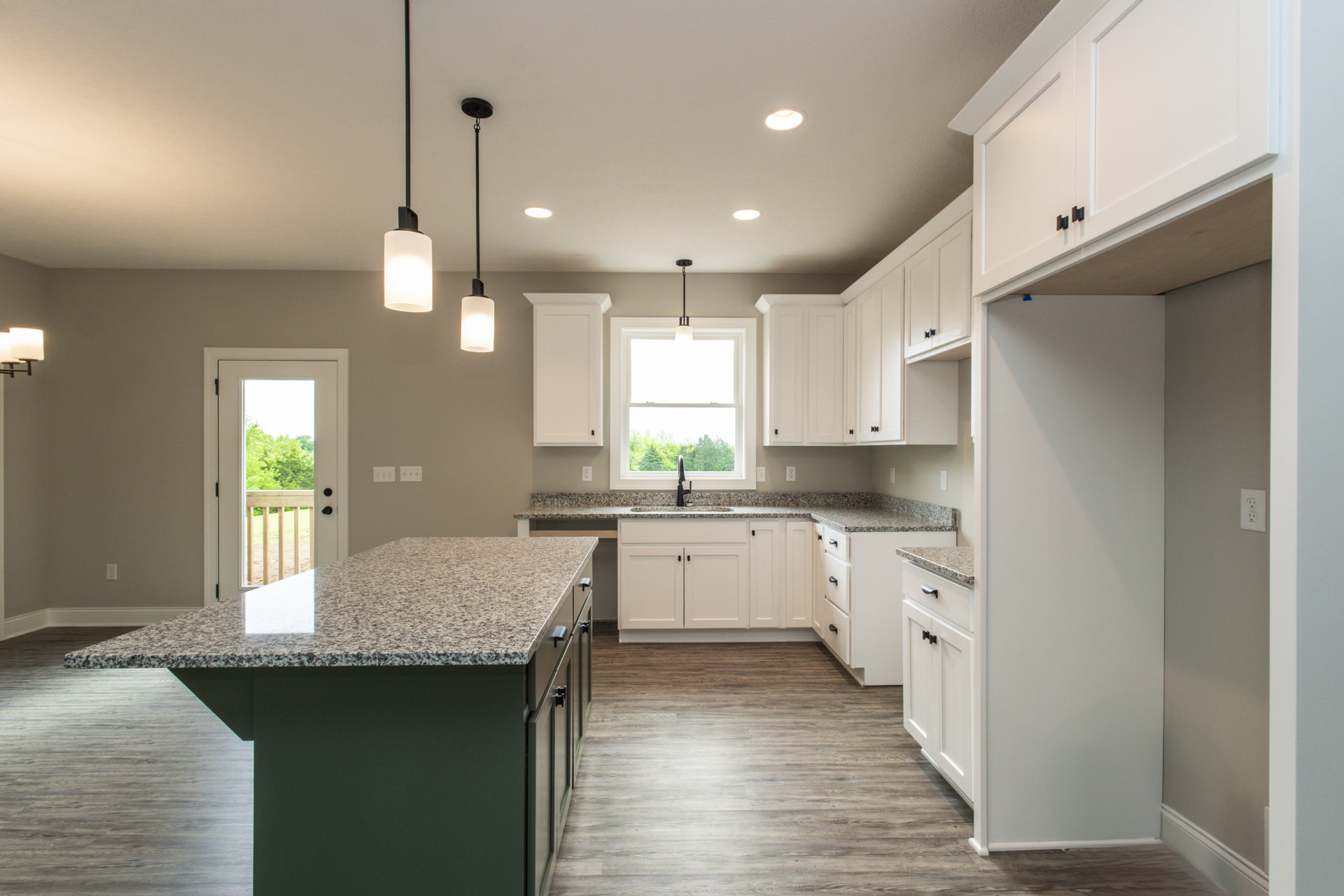 Granite countertops and white cabinetry in a kitchen with tile flooring, stainless steel sink beneath a window overlooking trees, pendant light fixture, and a door with glass panel