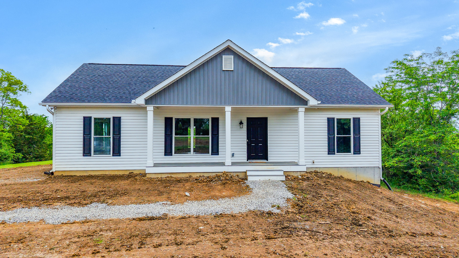 White modern home with blue roof, black front door, white walls, driveway, white-framed windows including one with decorative muntins, small tree and plants in front yard, partly