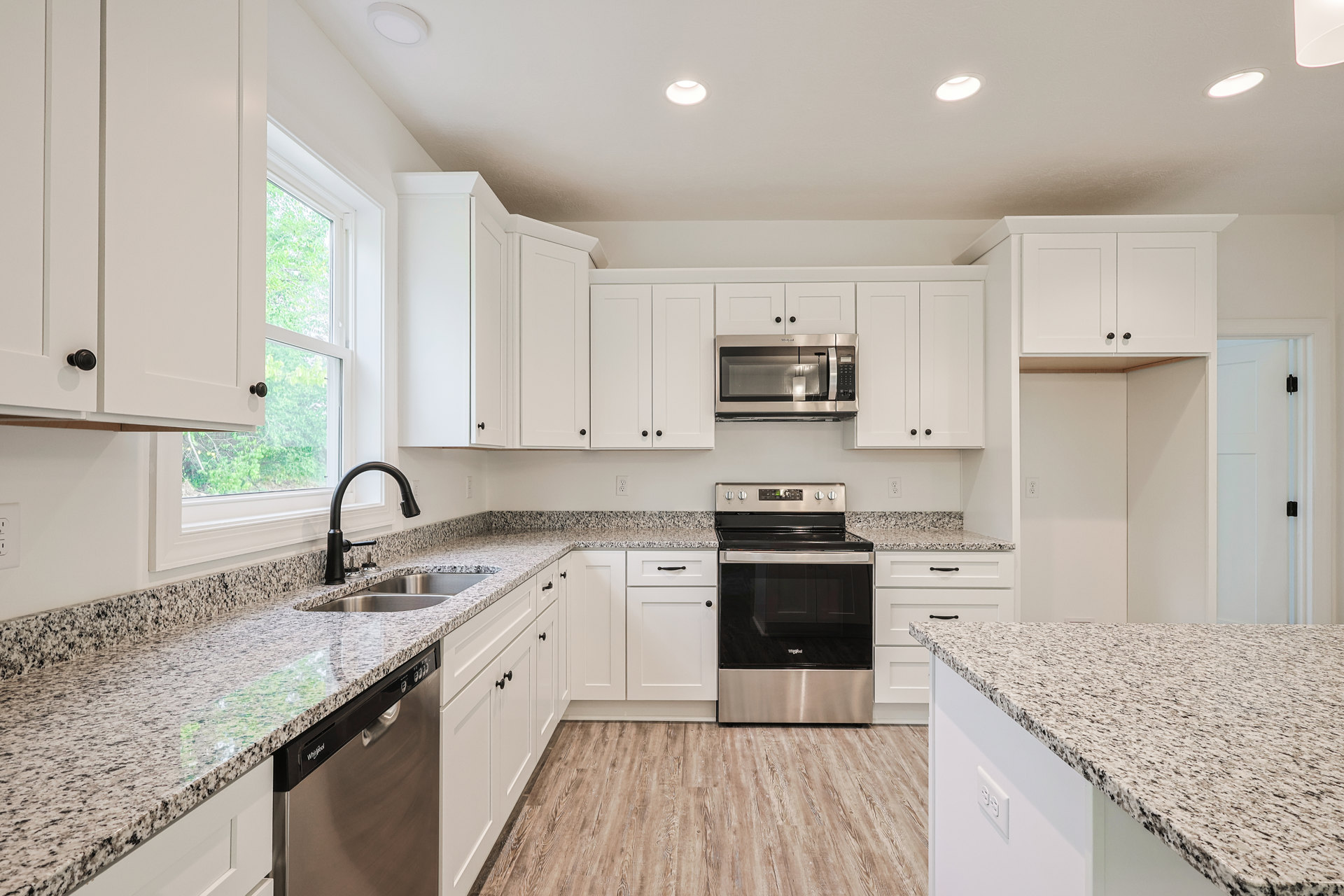 Granite countertops with white cabinetry, black faucet, stainless steel stove with glass door, built-in microwave, dishwasher, and marble counter adjacent to sink.