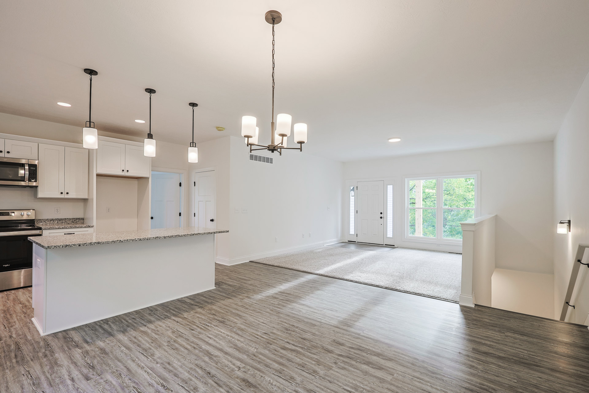 Kitchen with wood flooring, white cabinetry, stone countertop, black microwave, tile backsplash, sink, and chandelier; window overlooks trees.