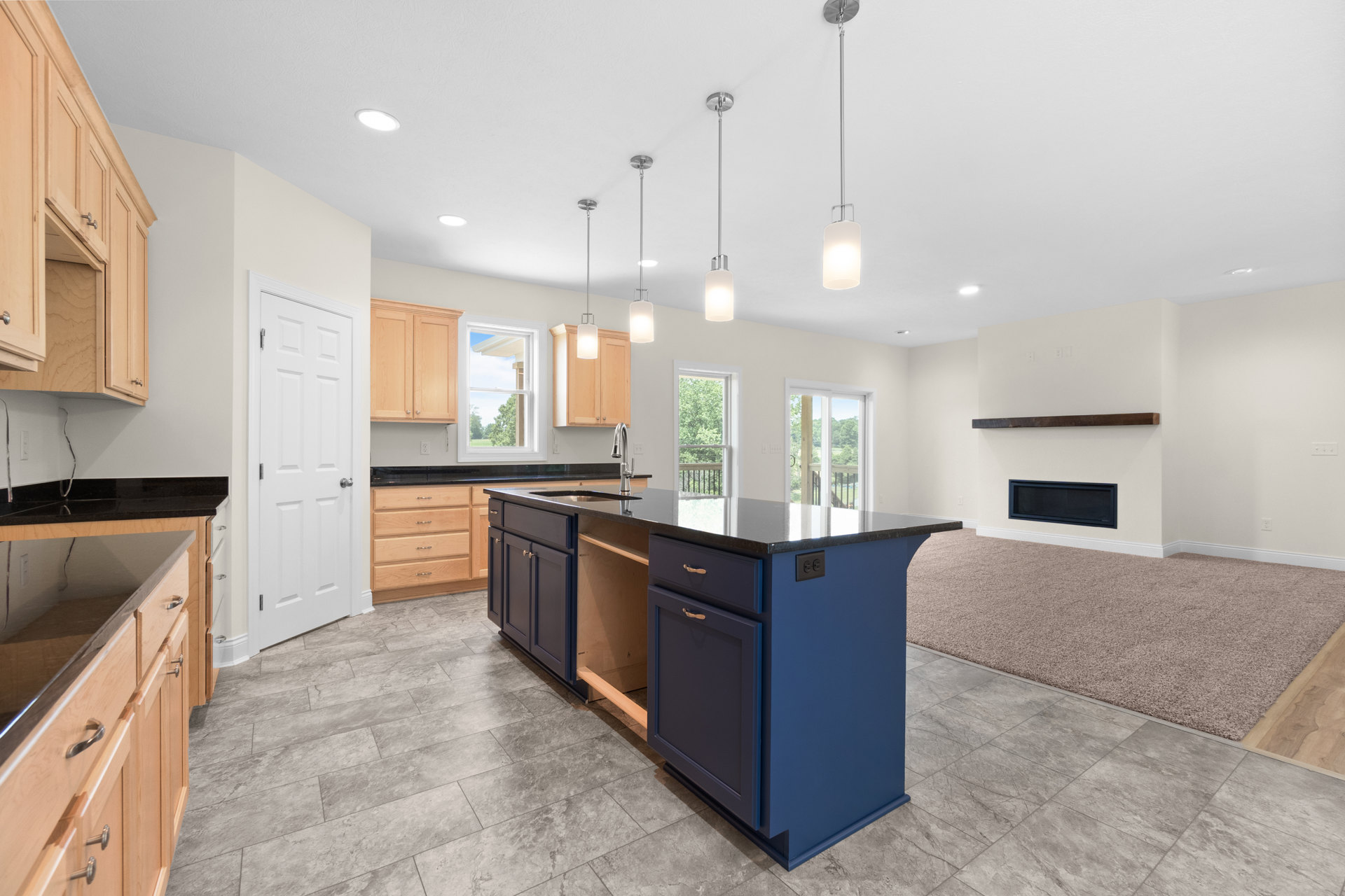 Blue kitchen island with built-in sink, white cabinetry and drawers, stainless steel hardware, white door with silver knob, window with white frame, long silver pendant light