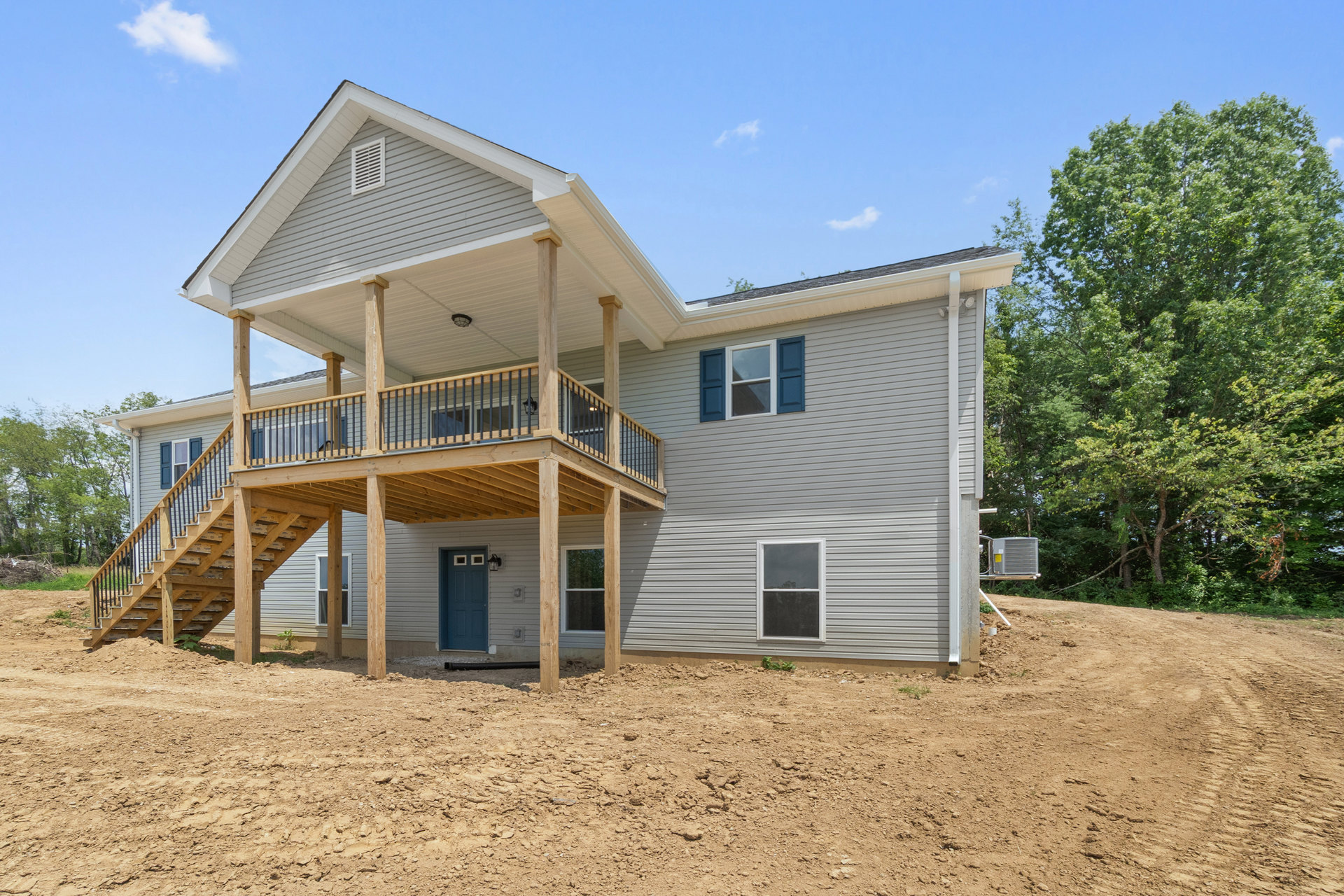 Wooden deck with blue door, white sign above entry, porch area, blue shuttered windows, tree beside house, dark evening sky