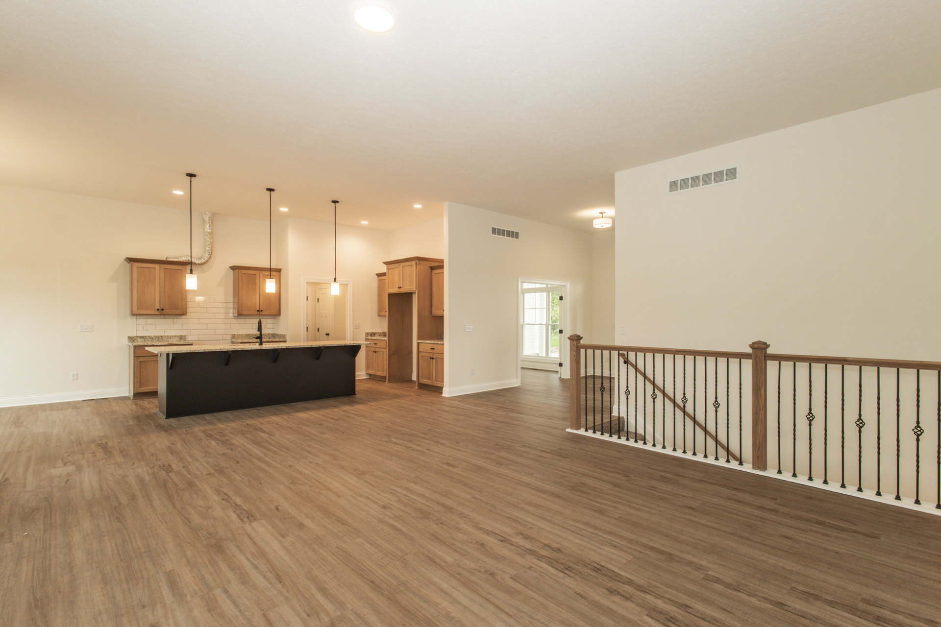 Open concept kitchen and living area with wood flooring, black countertop and faucet, staircase featuring wooden railing with metal balusters, white-framed window and door, and