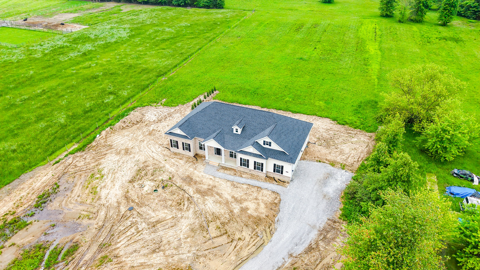Modern two-story house with light siding and dark roof, surrounded by lush green lawn, mature trees, and landscaped bushes