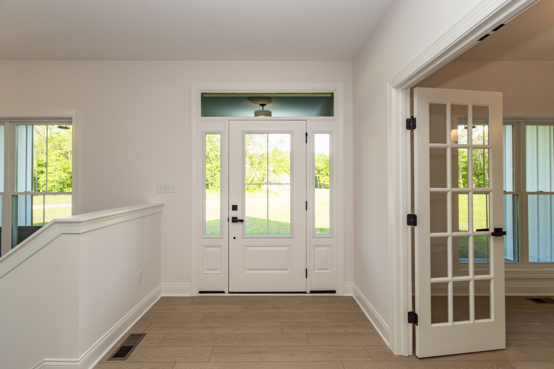 White paneled door with glass window panes, grey walls, wood flooring, and view of green lawn through glass.