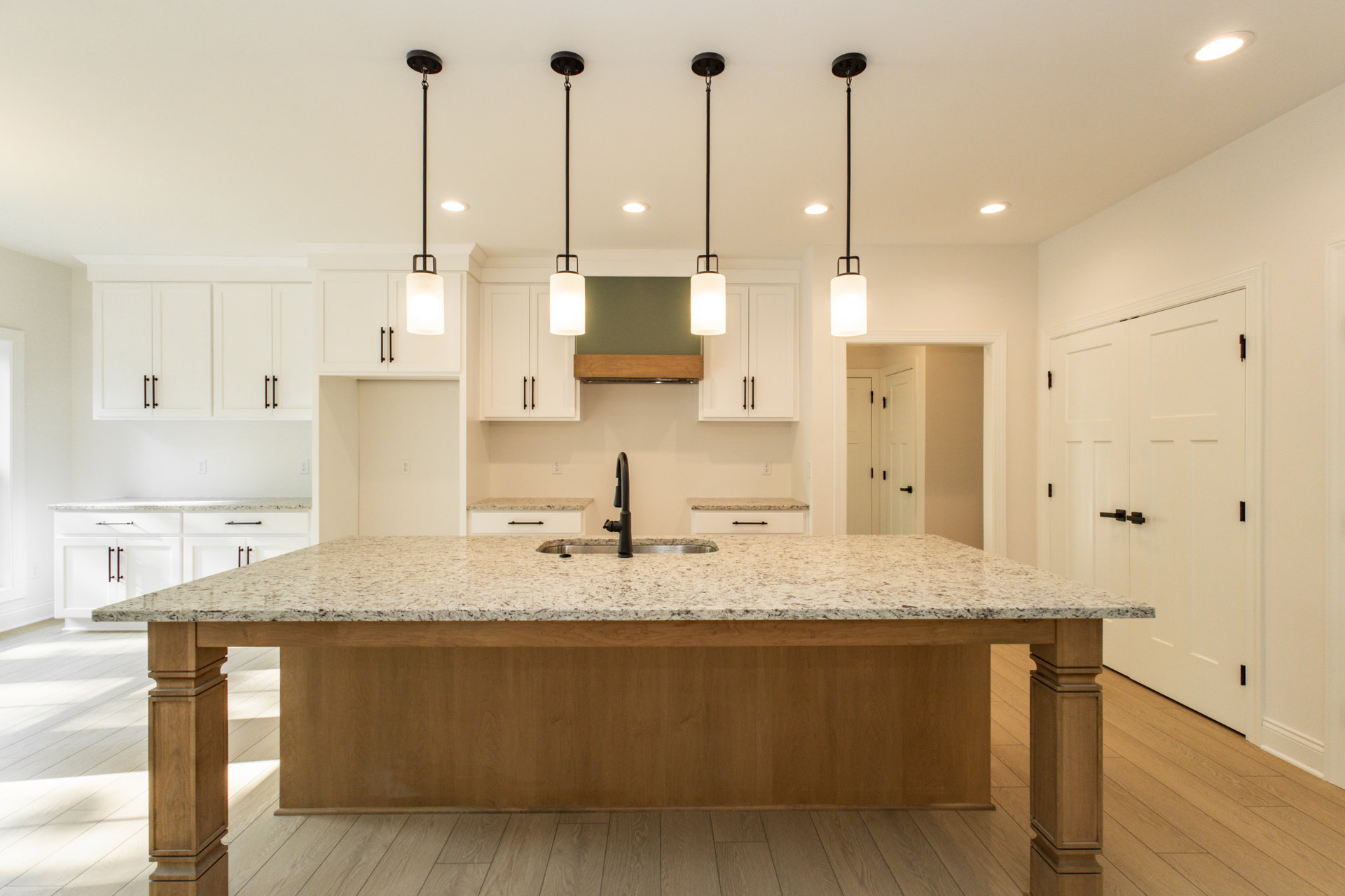 Spacious kitchen featuring a large central island with built-in sink, white tile backsplash, light wood cabinetry, pendant ceiling lights, and a black pipe accent on a white wall