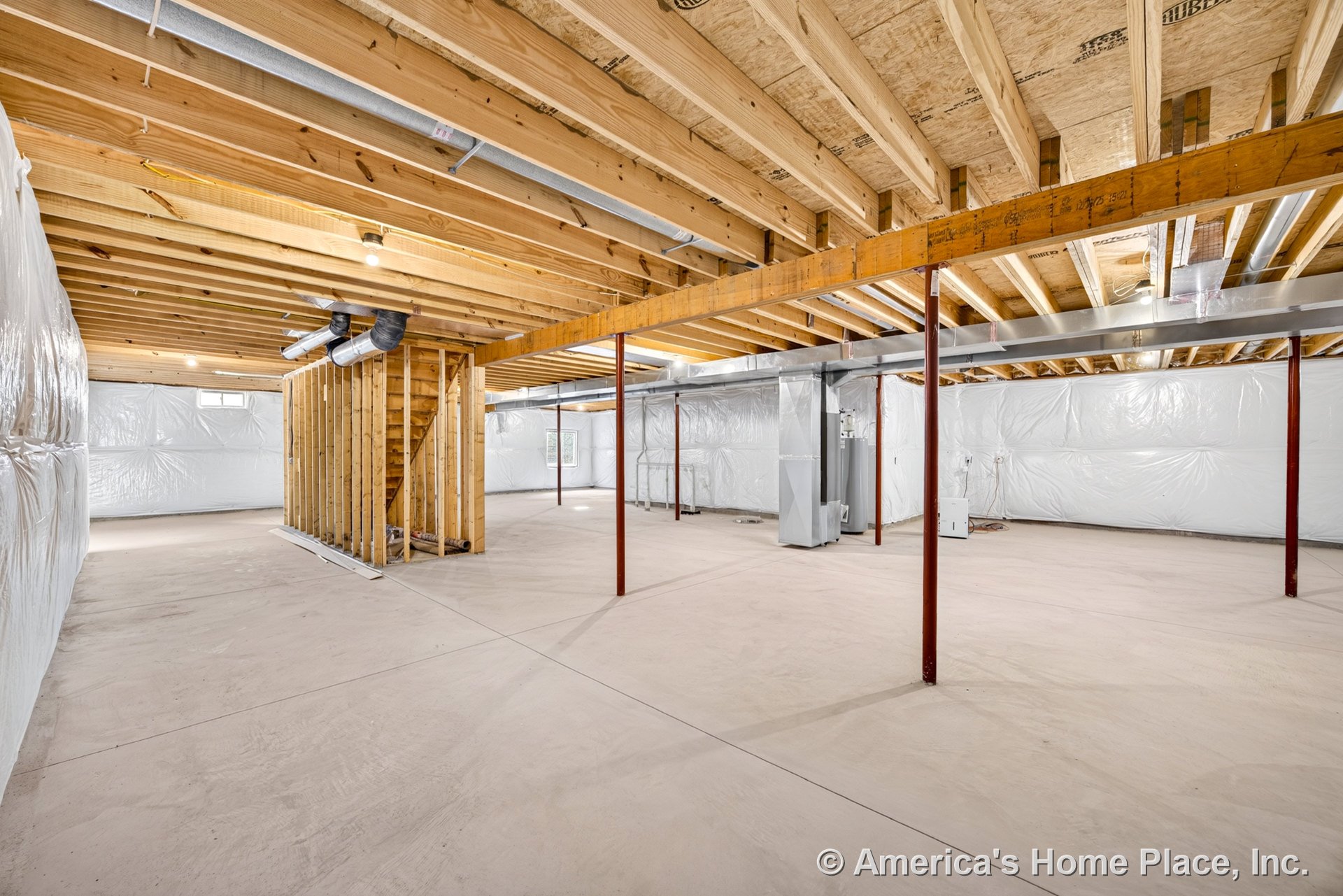 Unfinished basement with exposed wood ceiling joists, concrete slab floor, wrapped wall insulation, metal support columns, open staircase framing, visible HVAC ductwork, and