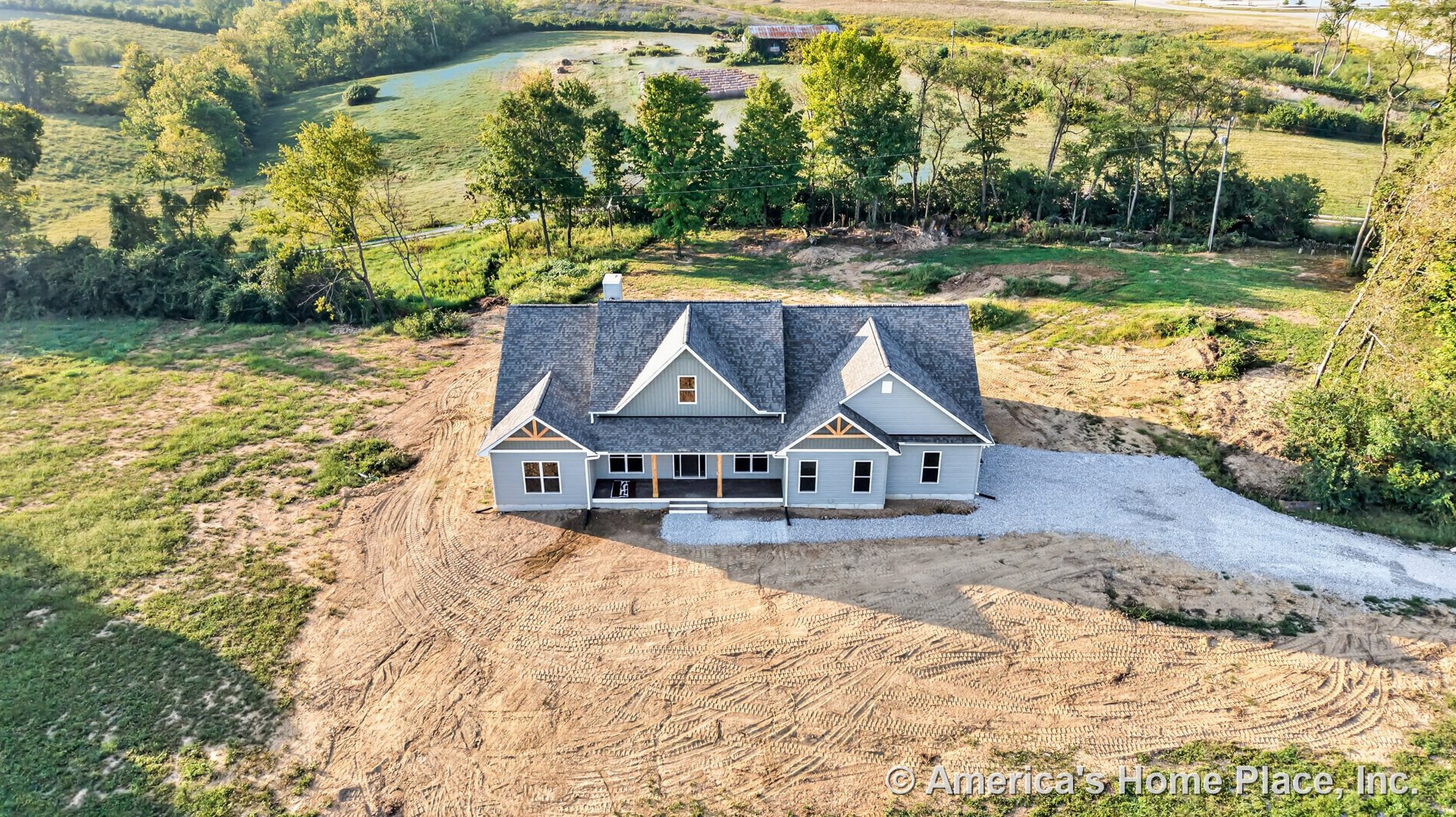 Modern farmhouse exterior with gray horizontal siding, multiple gabled rooflines, covered front porch supported by wood accent beams, white trim framing windows, and gravel