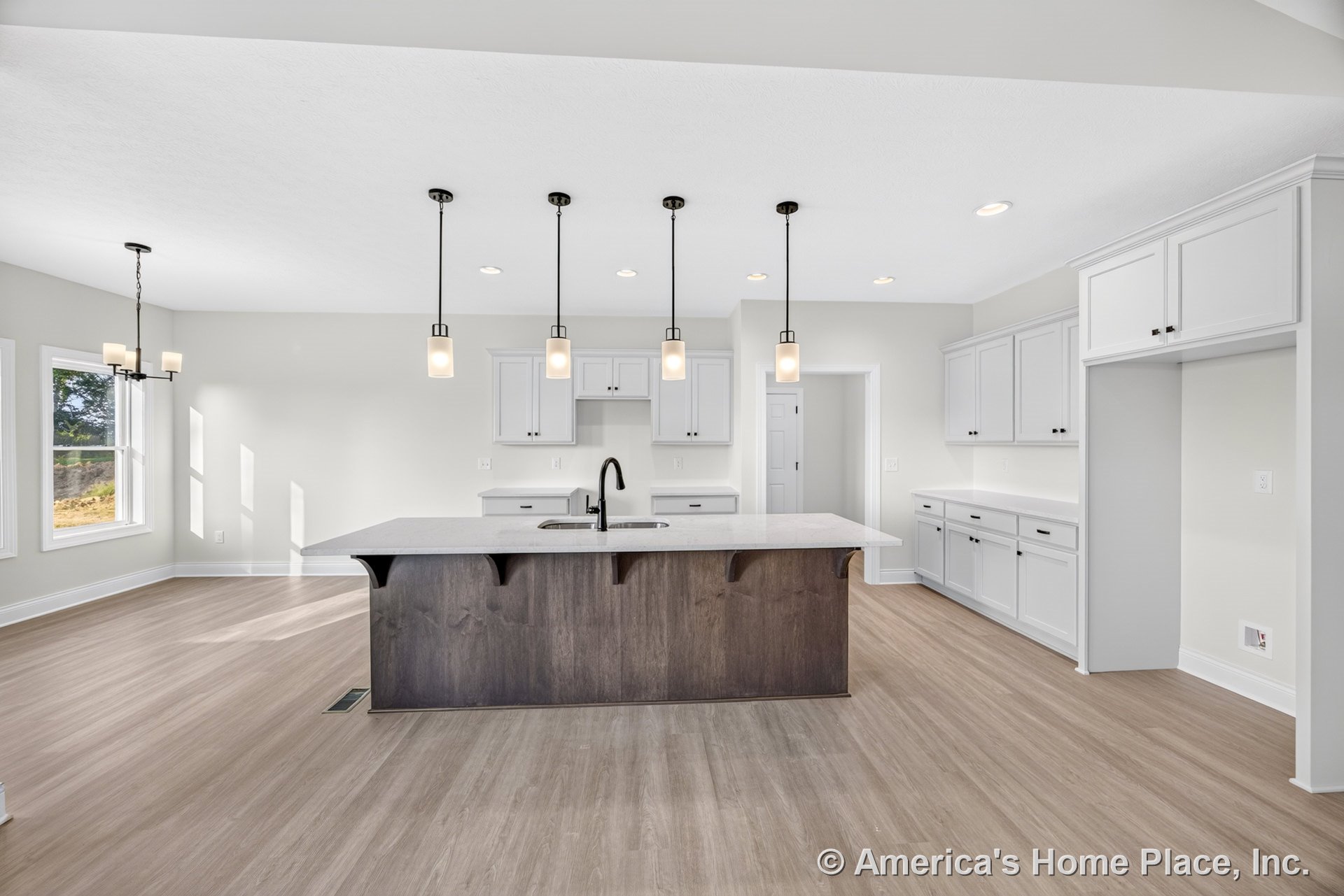 Large central kitchen island with quartz countertops, surrounded by white shaker cabinets, pendant lights above the island, light wood flooring, recessed ceiling lights, and