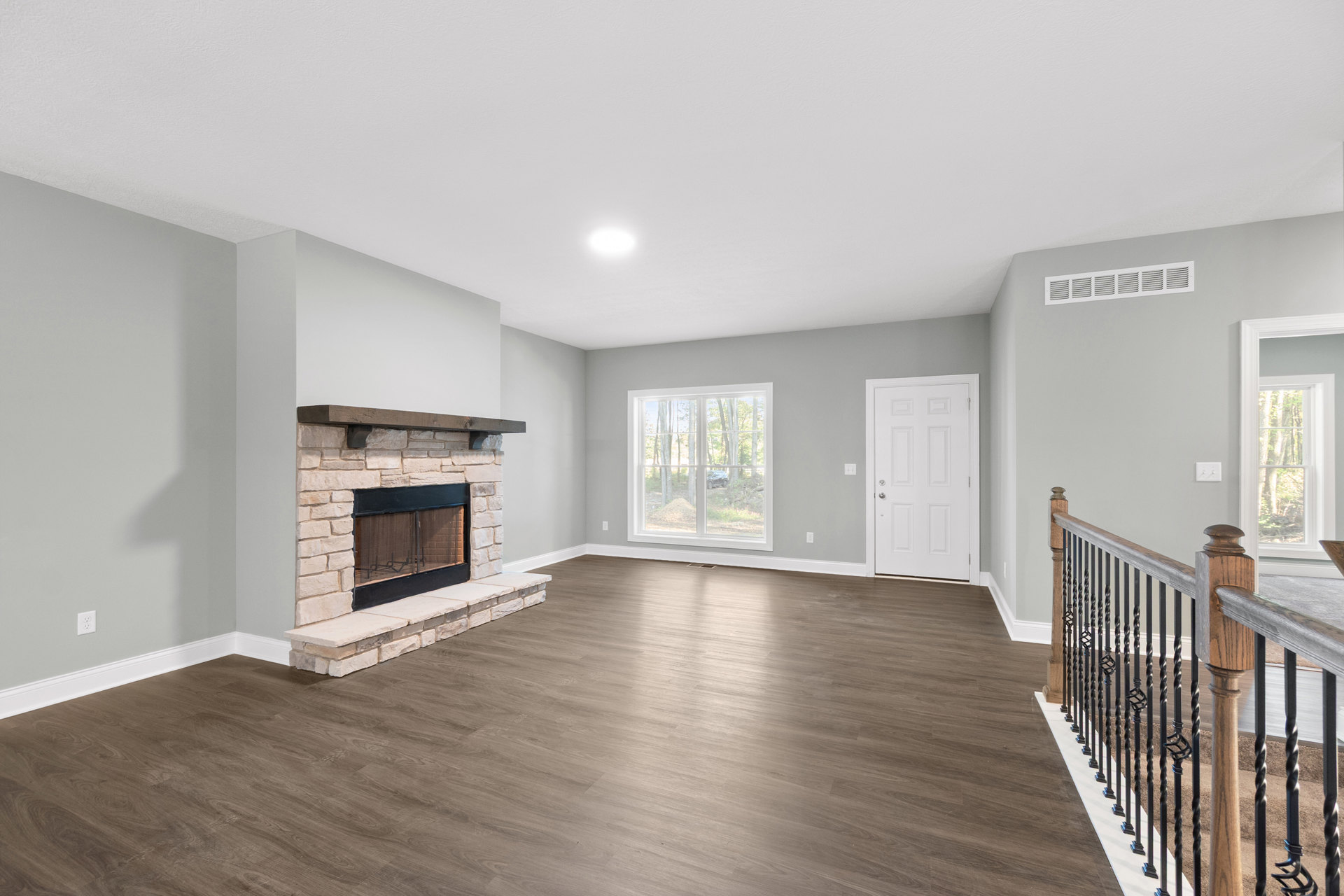 Living room with hardwood flooring, white fireplace featuring a wood mantel, white door with silver handle, window showing parked car outside, close-up of metal railing