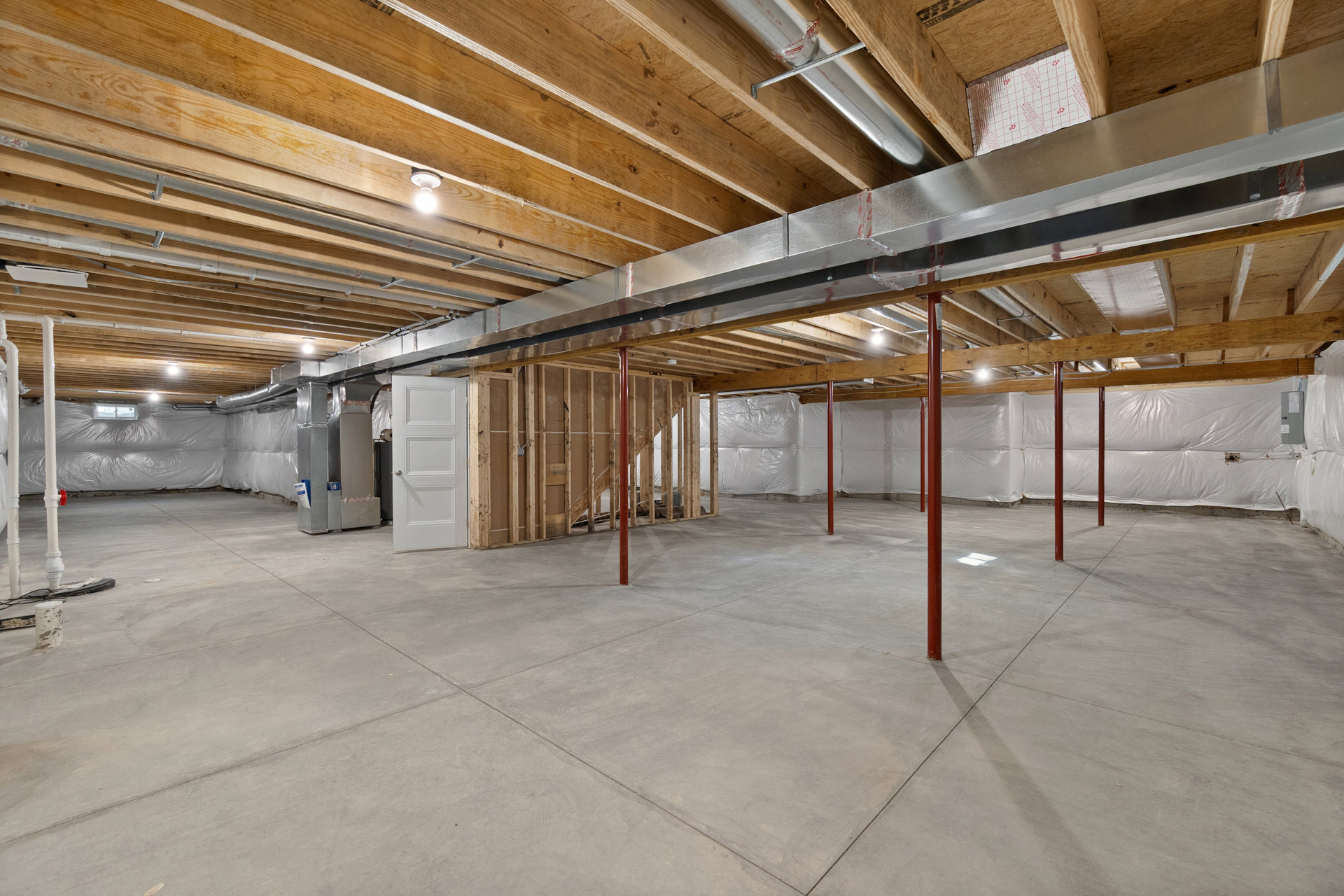 Basement room with exposed steel beam and metal ceiling, concrete floor with red support poles, white door with silver handle, light bulb on wood surface, and paper with red