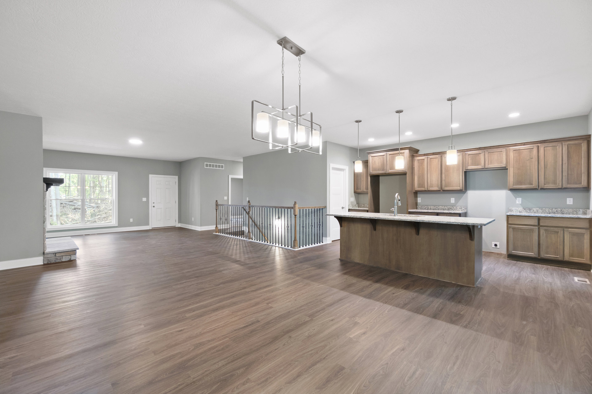Open-concept kitchen with marble island, stainless steel faucet, wood flooring, white cabinetry, silver door handle, large window overlooking forest, and modern metal railing