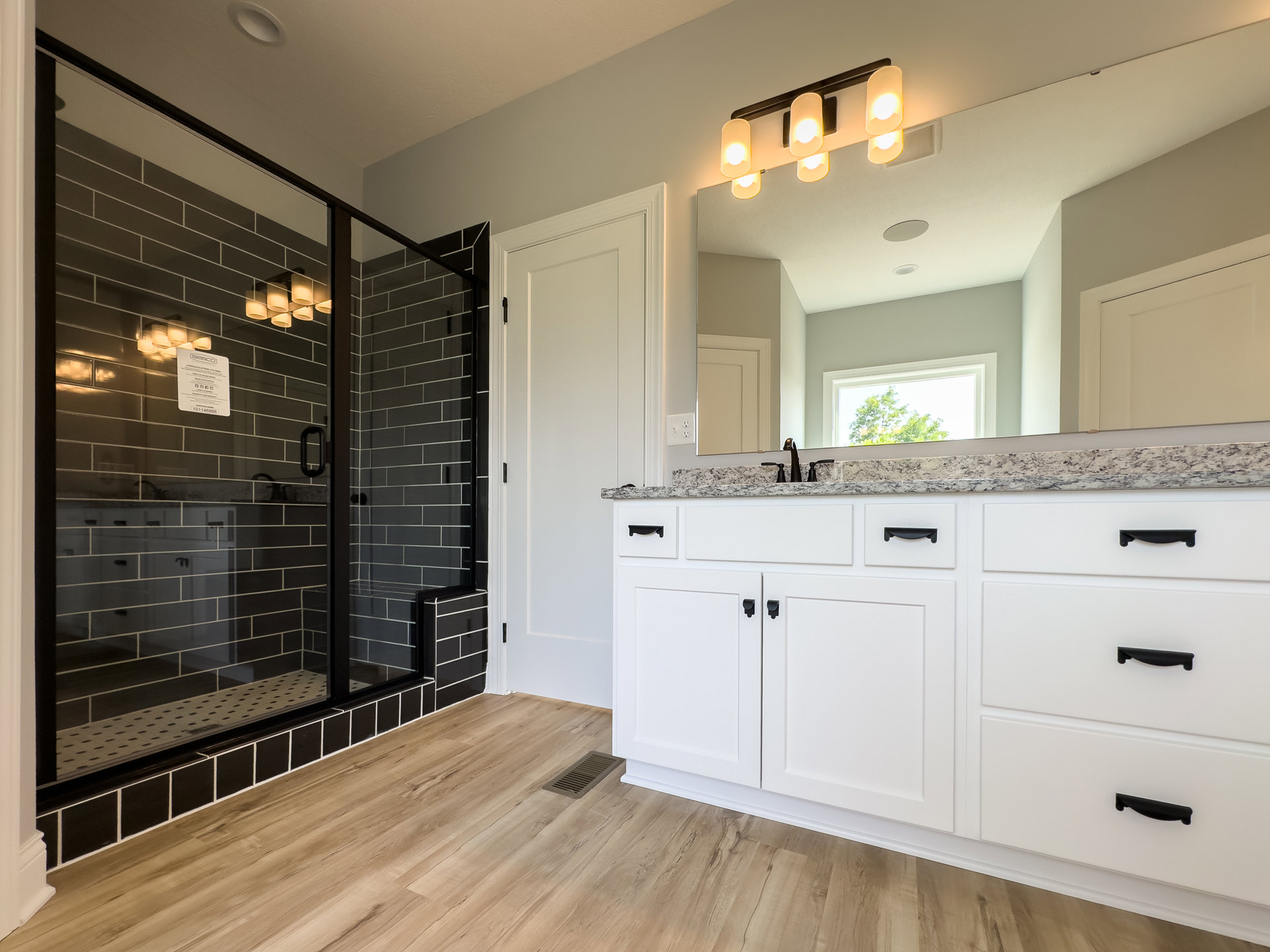 Bathroom featuring a frameless glass shower enclosure, white vanity with undermount sink, black hardware, and modern wall-mounted light fixtures.