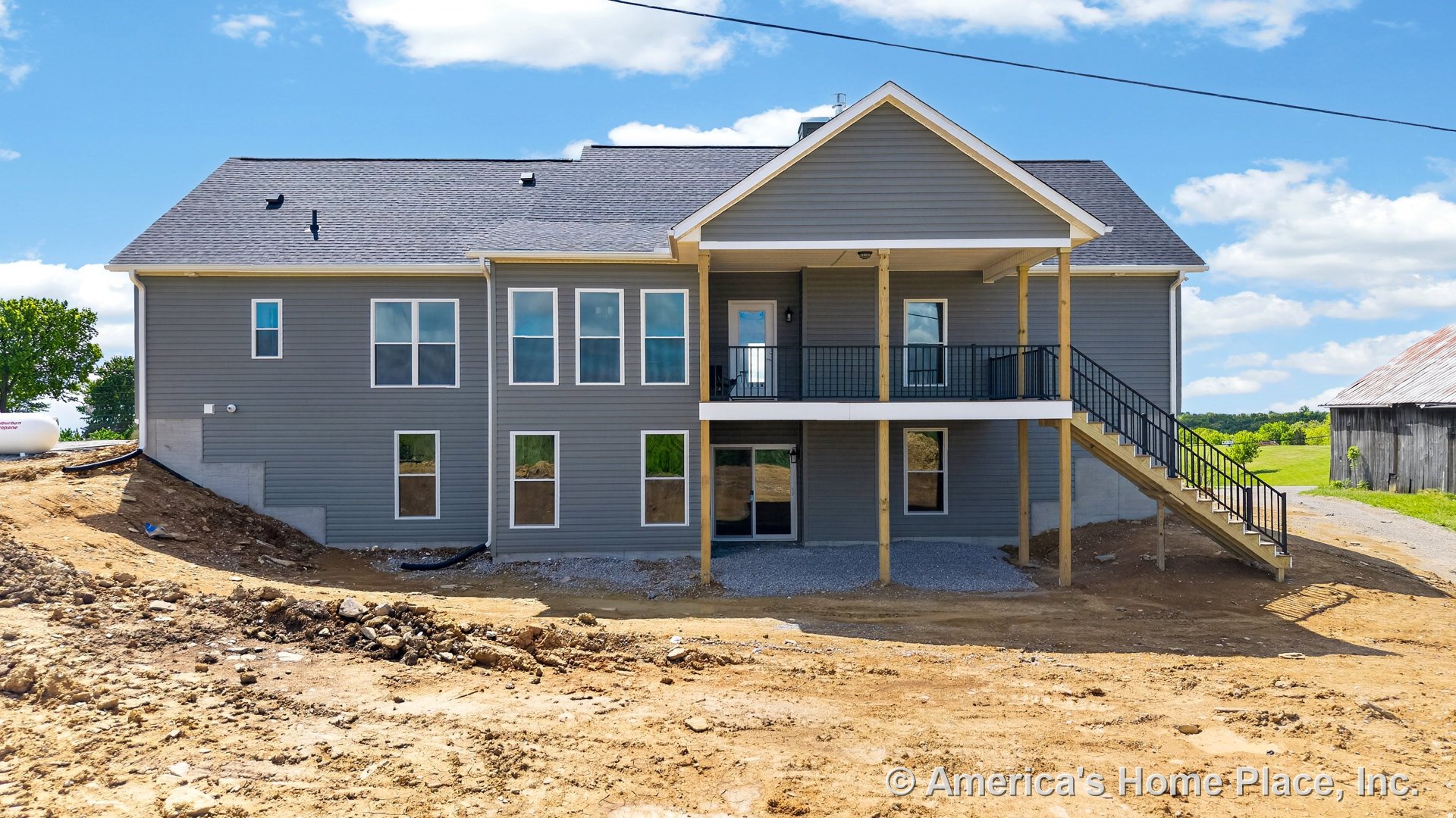 Gray vinyl siding exterior with double-hung windows, covered upper porch supported by wooden posts, metal railing staircase leading to walk-out basement entry, and contrasting roof