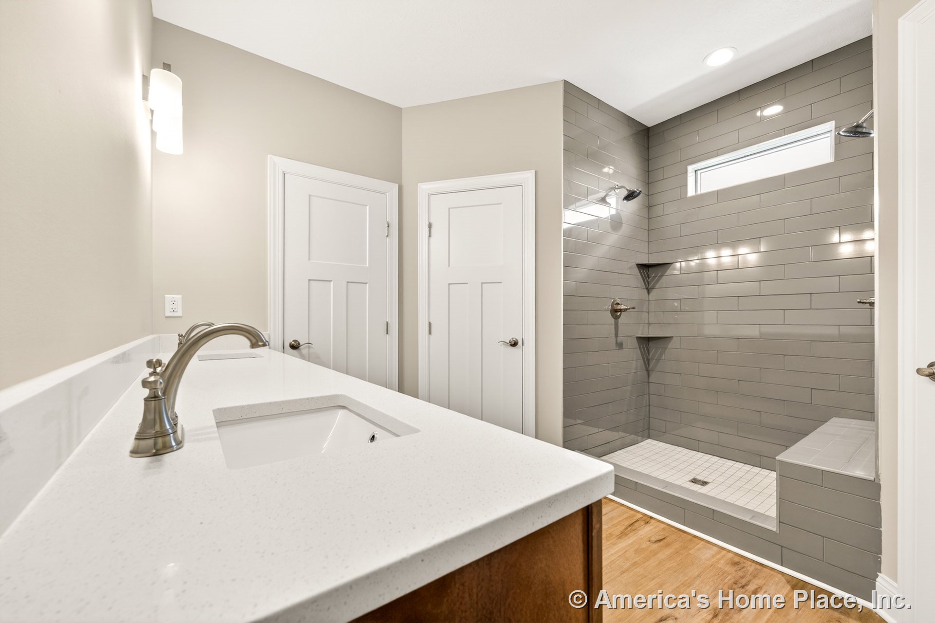 Walk-in shower with gray subway tile, built-in tile niche, and bench seat; double vanity with quartz countertops, modern fixtures, wood cabinetry, recessed lighting, white paneled