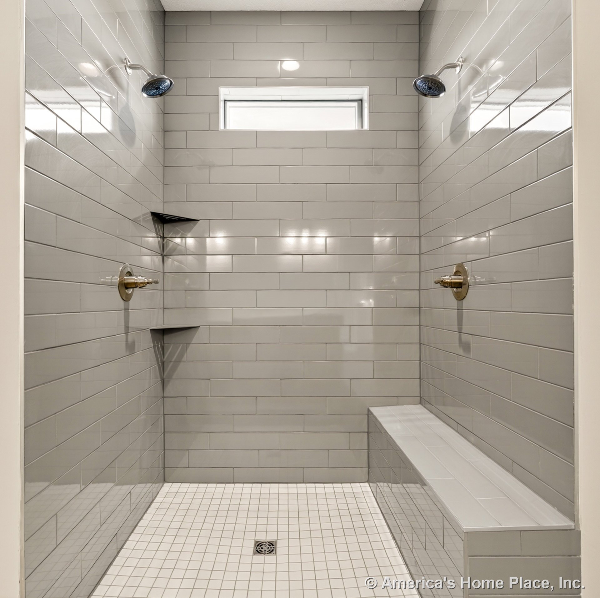 Walk-in shower with gray subway tile walls, dual showerheads, built-in bench, recessed wall niches, small window for natural light, and white square tile flooring