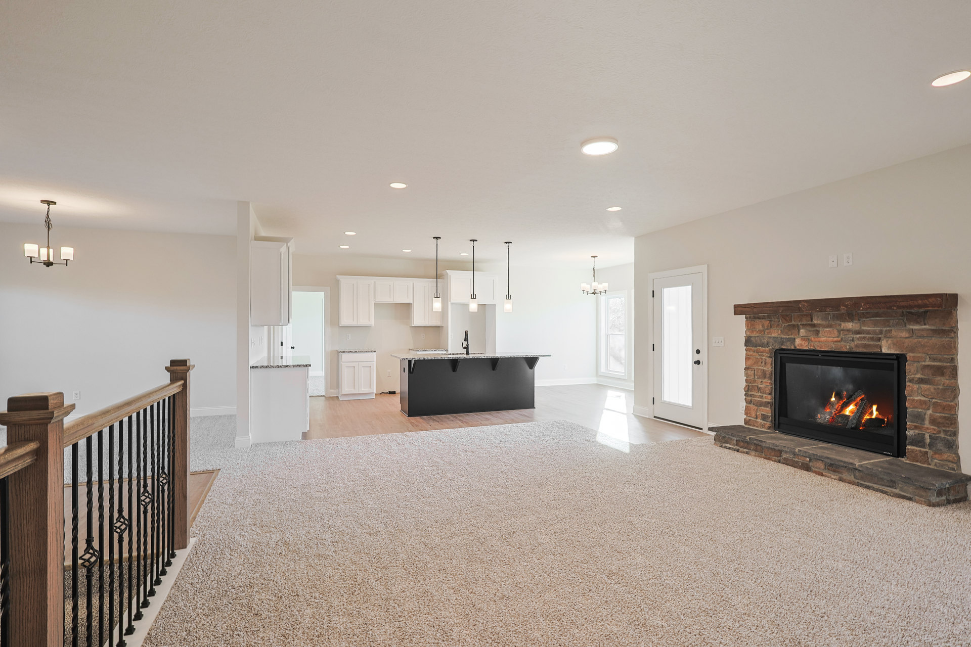Open concept living room with wood-burning fireplace, marble kitchen island, black countertop, white door, and metal railing