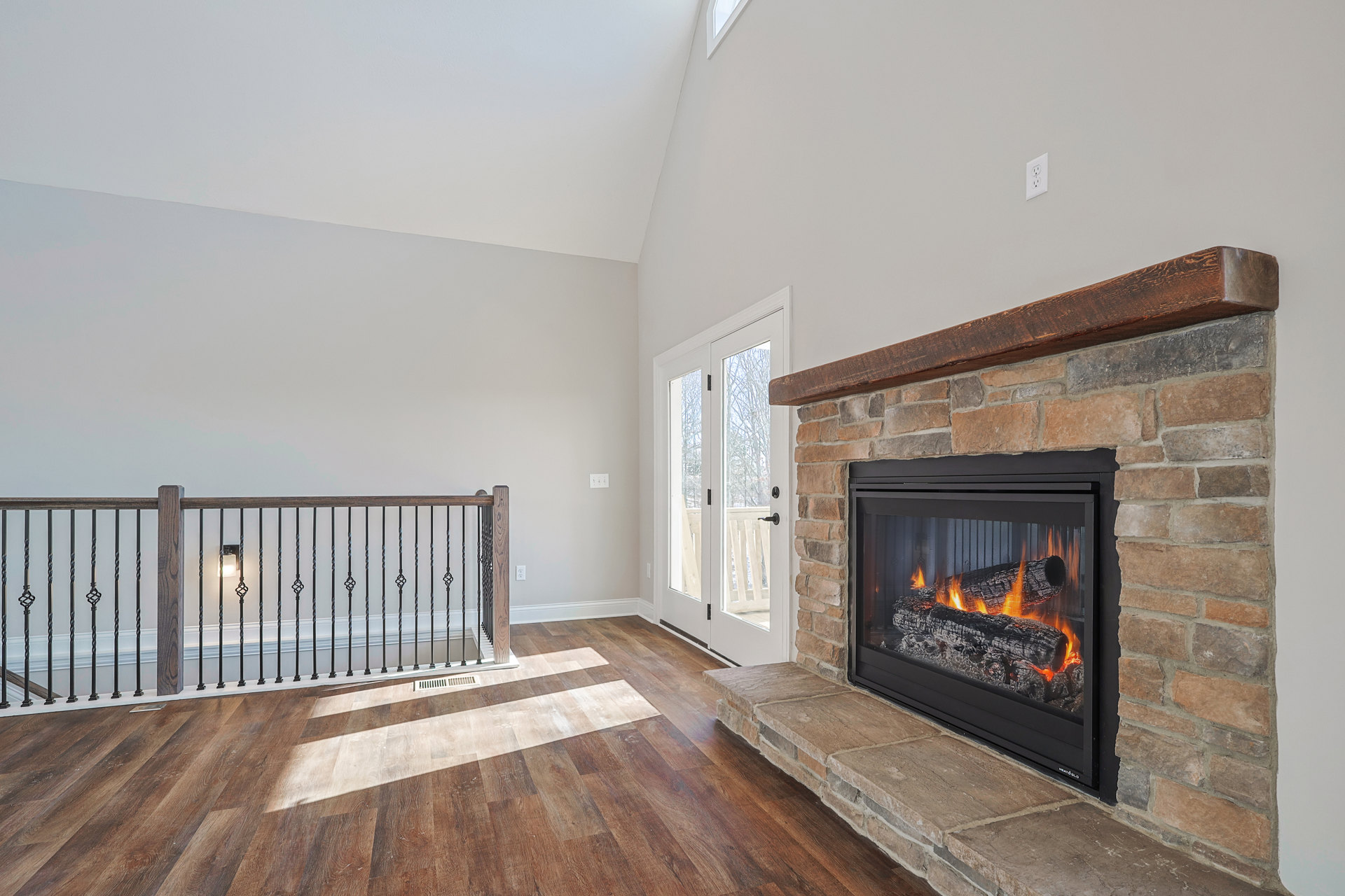 Stone fireplace with glass doors, burning logs, and fire screen in a living room with hardwood floors and neutral walls