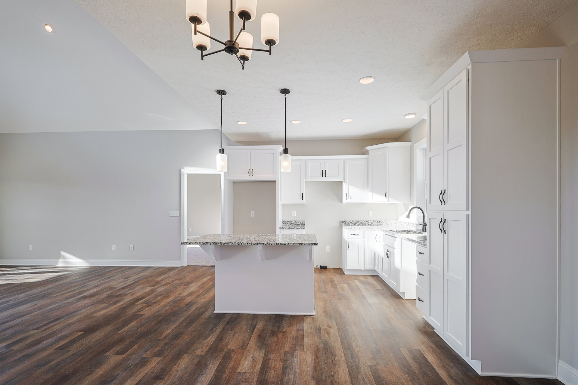 Kitchen with black-speckled white granite countertop, wood flooring, white cabinetry, and chandelier with white shades