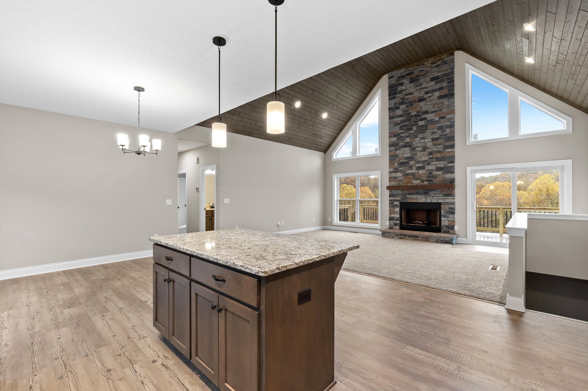 Spacious living room featuring a stone fireplace with black frame, large kitchen island with granite countertops, tile flooring, white cabinetry, rectangular ceiling light, and