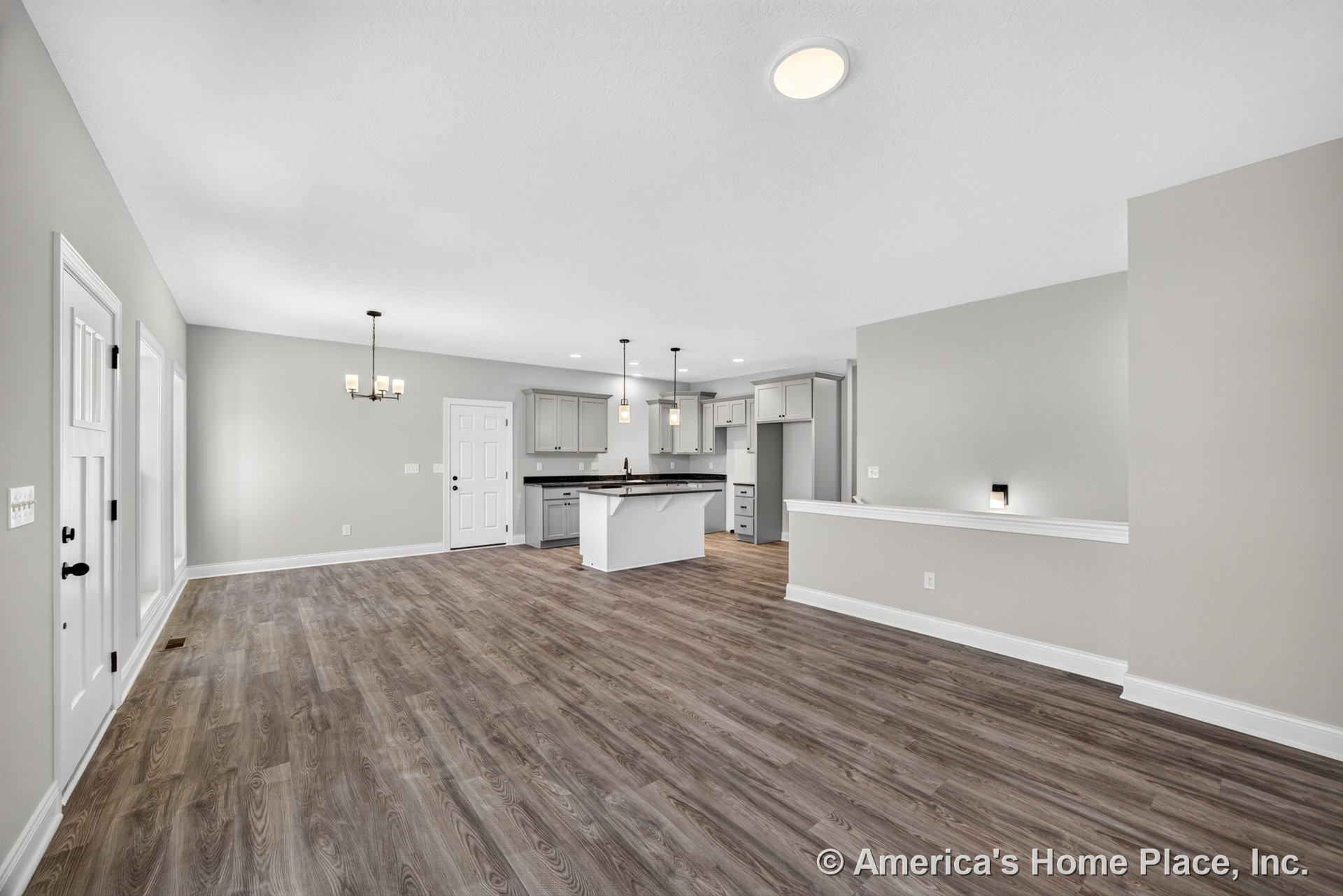 Open-concept kitchen and living area with gray shaker cabinets, pendant lights above the island, wood-look vinyl plank flooring, recessed ceiling lights, white trim and baseboards