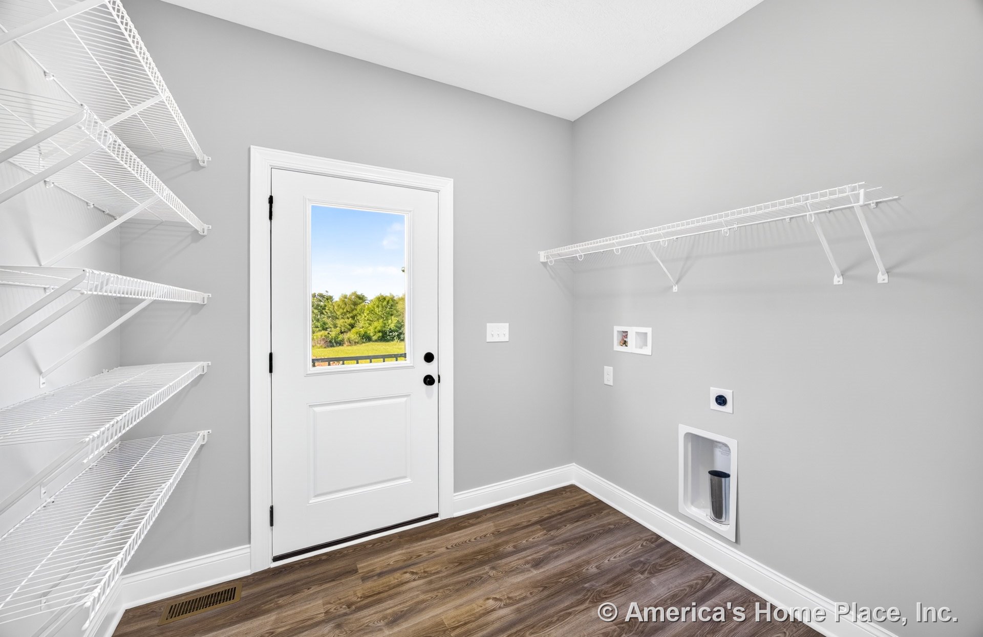 Utility pantry with white wire shelving, laundry appliance hookups, gray painted walls, wood-look vinyl flooring, white baseboard trim, and an exterior door featuring a window.