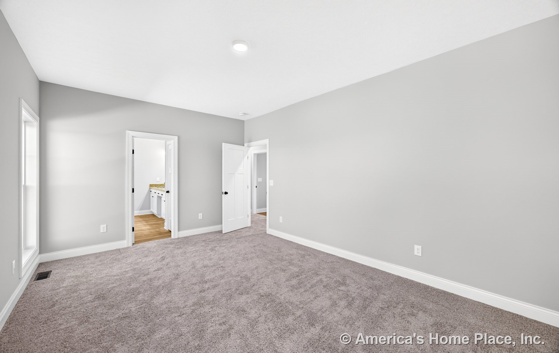 Bedroom with light gray carpet, soft gray walls, white baseboards and trim, recessed ceiling light, two white paneled doors to adjacent rooms, and a large window with white trim.