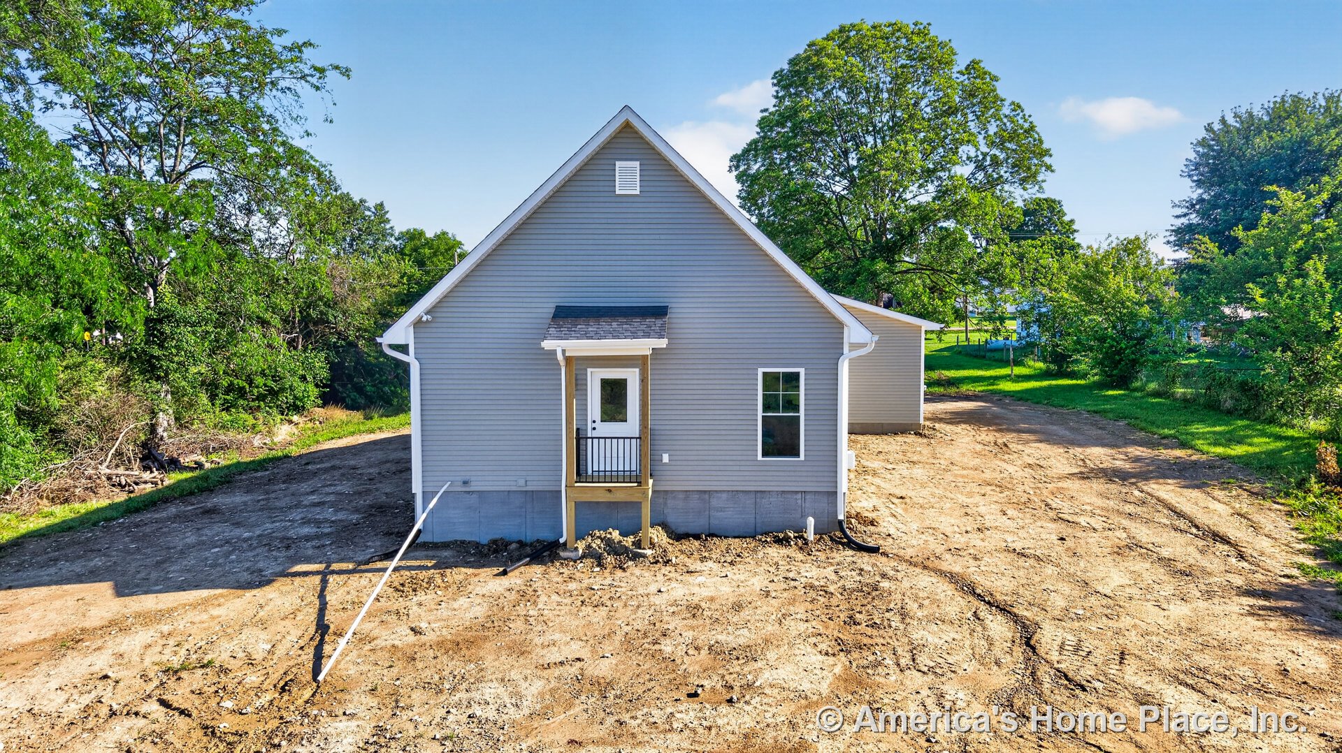 Gray vinyl siding with white framed windows, gable roof, small covered rear porch featuring black metal railing, single entry door, concrete foundation, white trim, and downspout.
