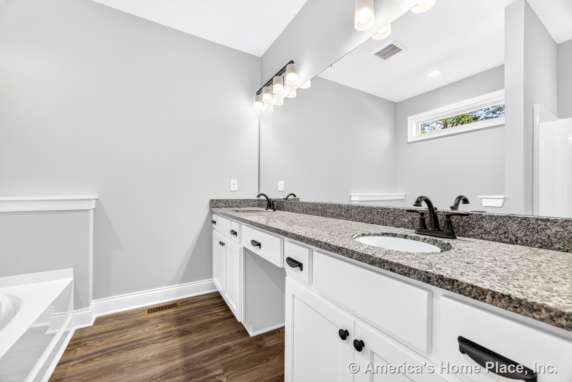 Double vanity with granite countertop, white shaker cabinets, matte black faucets, large wall mirror, wall-mounted lighting, wood-look flooring, neutral wall color, window, and