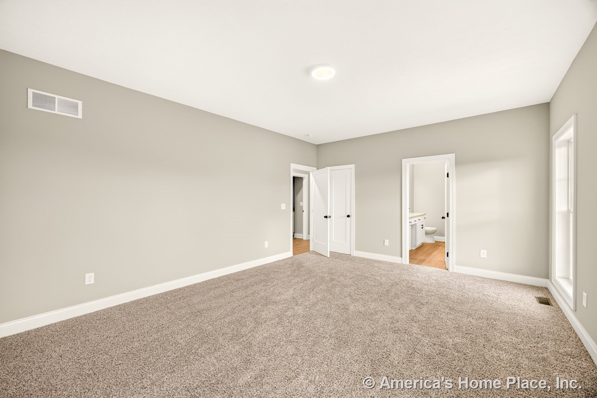 Master bedroom with light beige carpet, soft gray walls, white baseboards, and a flush ceiling light; double doors lead to a closet, and an open entry reveals the en suite bathroom