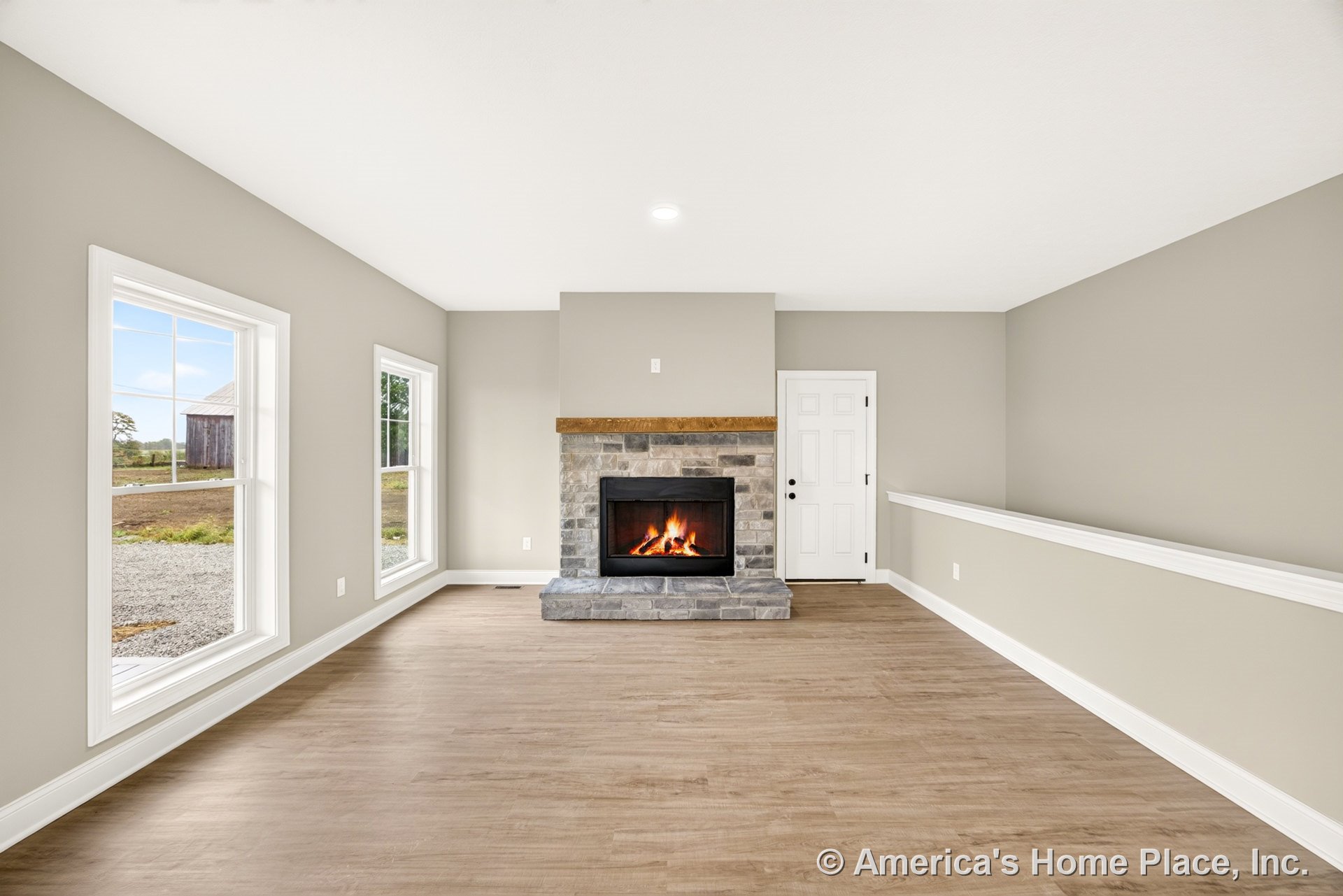 Stone fireplace with wood mantel centered on one wall, surrounded by large double-hung windows with white trim and baseboards, light wood flooring, neutral wall paint, and recessed