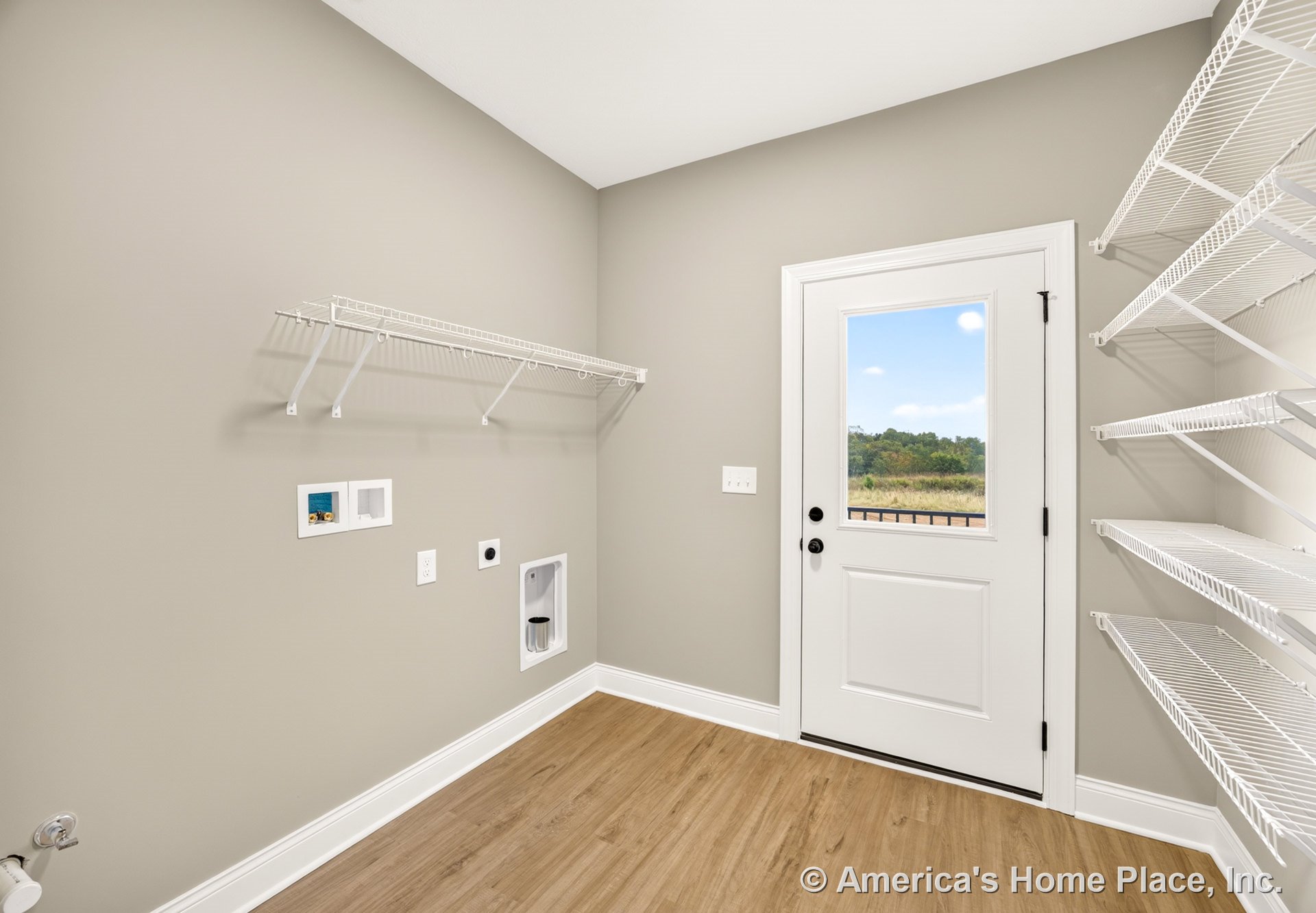 Utility pantry with wire wall shelving, laundry appliance hookups, white exterior door with glass insert, light wood-look vinyl flooring, neutral painted walls, and baseboard trim.