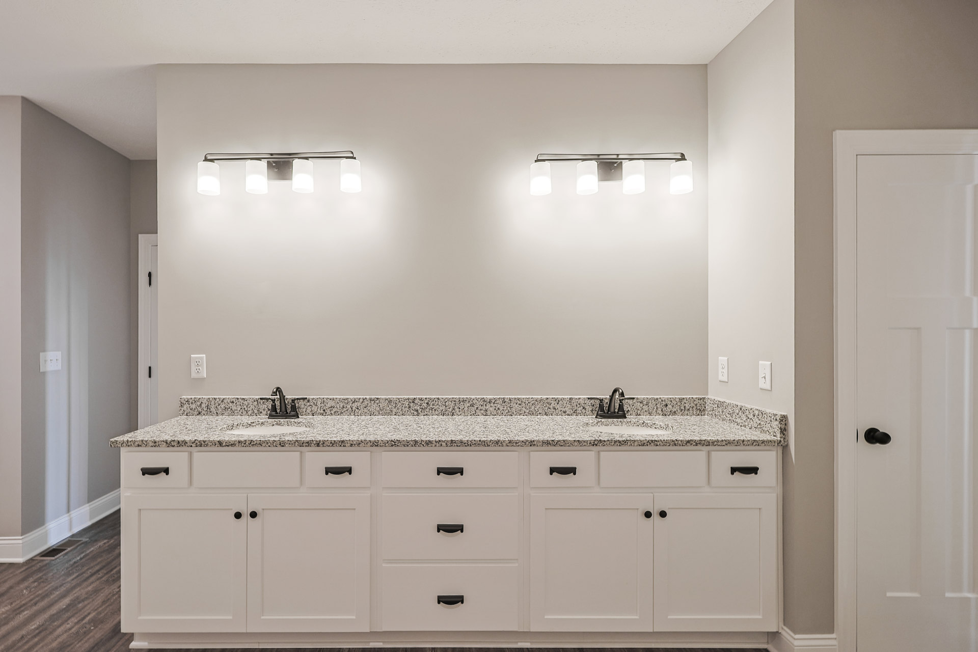 White bathroom with marble countertops, white cabinetry, chrome faucet, black door handle, wall-mounted lights, tile flooring, and drawers beneath the counter.