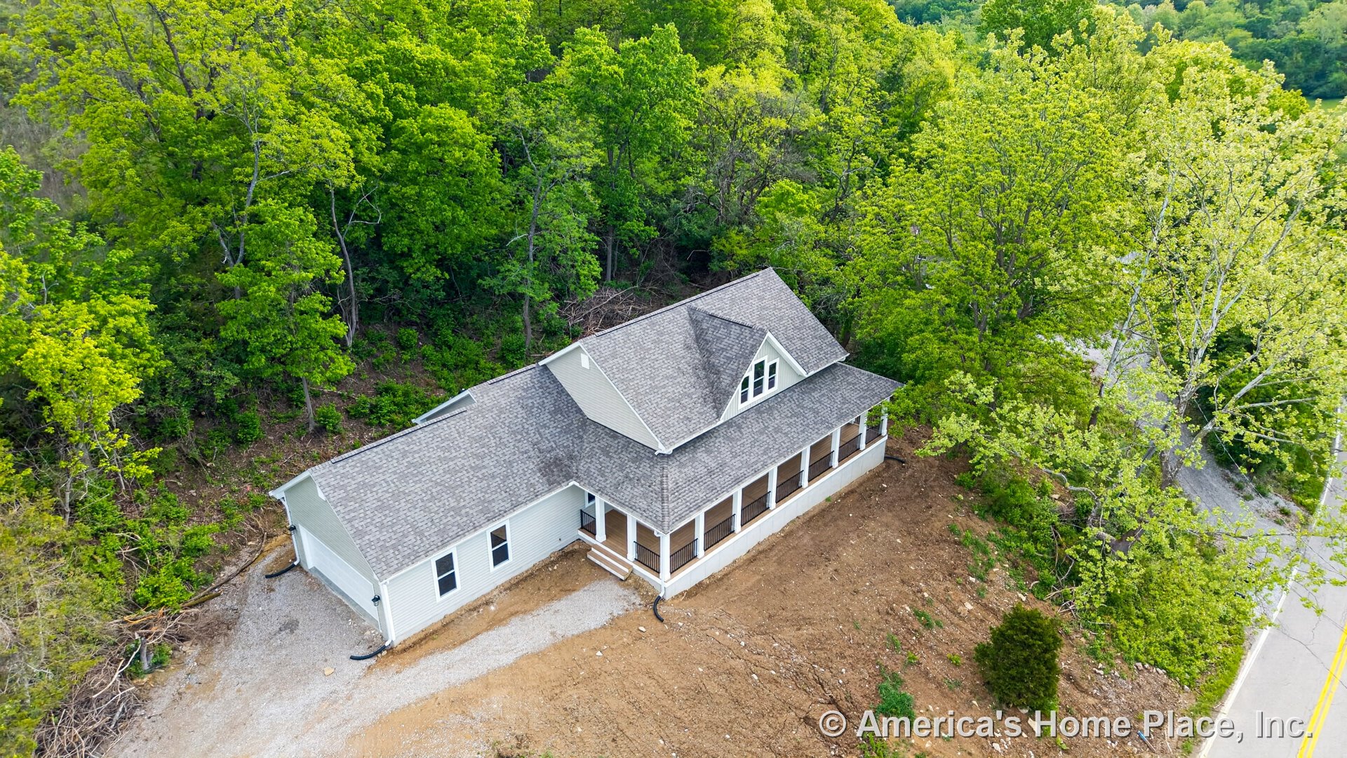 Large covered front porch with white trim and black railings, multiple gable roof, white exterior siding, double front entry doors, gravel driveway, and prominent front steps.
