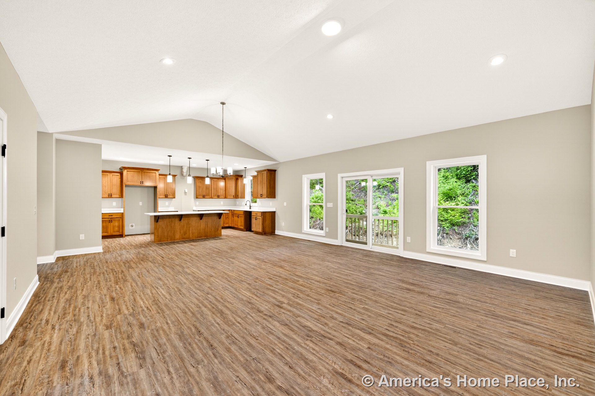 Open concept living area with vaulted ceiling, recessed lighting, wood-look plank flooring, large windows and glass door to porch, kitchen featuring natural wood cabinetry, white