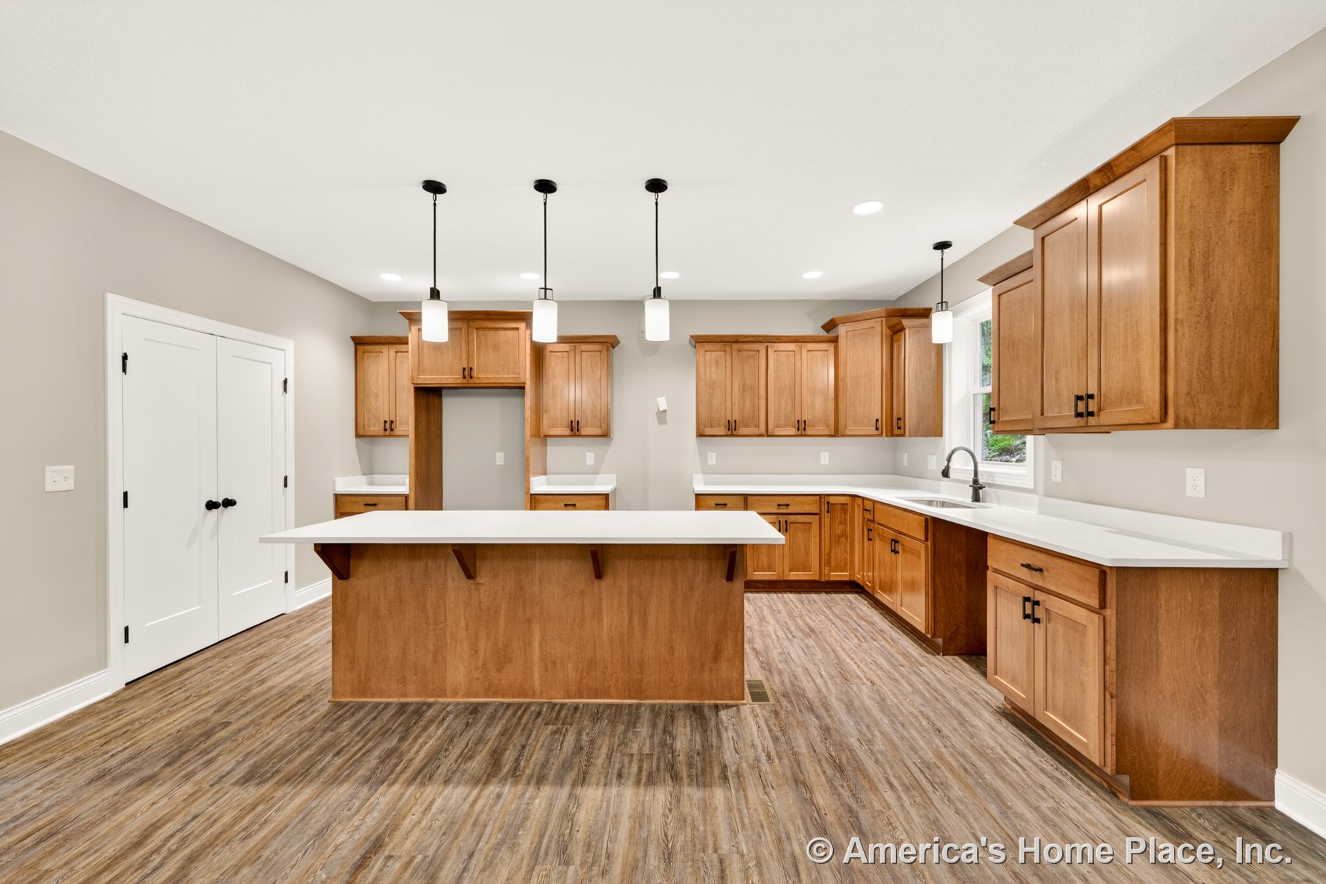 Wood shaker cabinets with white solid surface countertops, central island illuminated by pendant lights, double door pantry, large window above sink, wood-look vinyl flooring