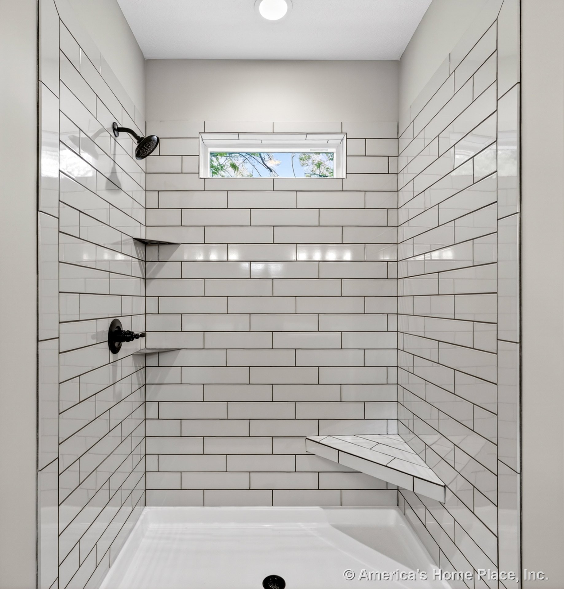 White subway tile shower with built-in corner bench, recessed niche, matte black fixtures, rectangular window, and overhead recessed lighting.
