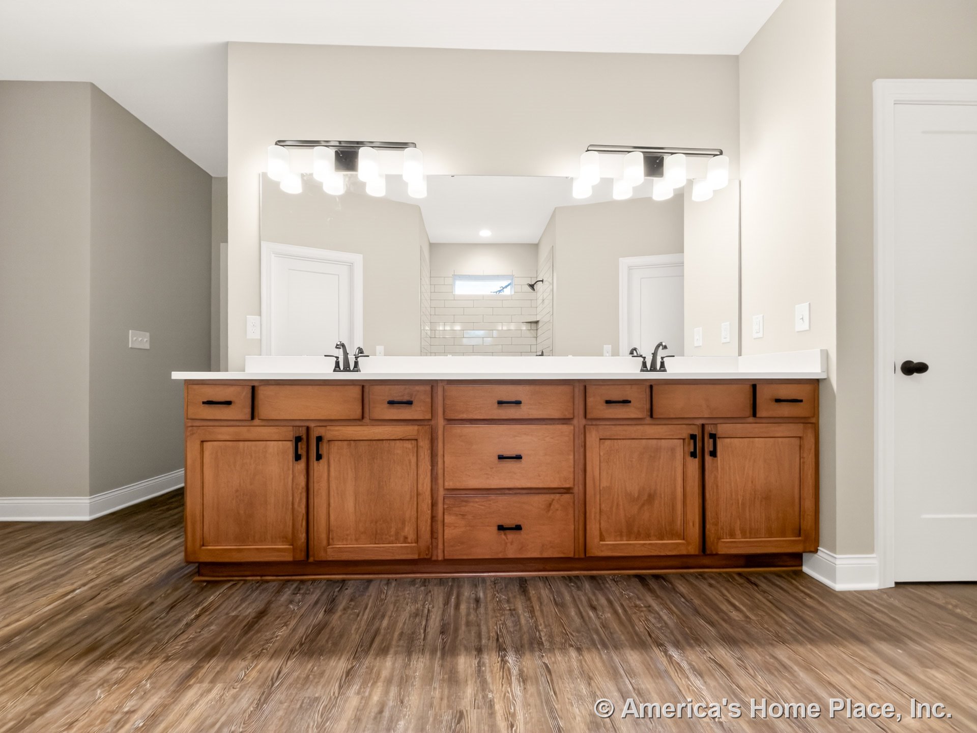 Double-sink vanity with wood cabinetry and white solid surface countertop, dual undermount sinks, wall-mounted modern light fixtures above a large wall mirror, wood-look tile