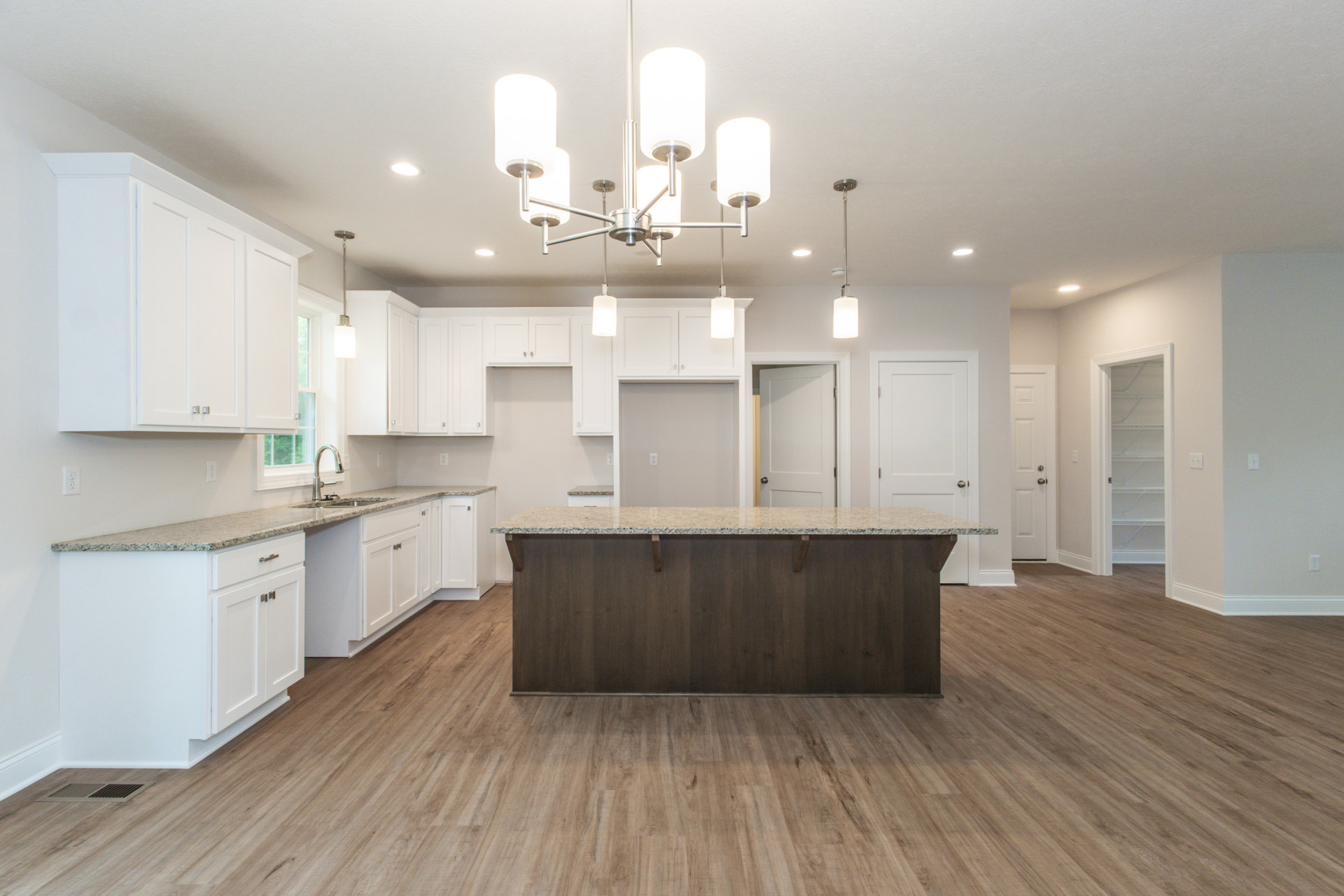 Spacious kitchen featuring a large wood-surface island, wood flooring, white cabinetry, stainless steel sink, and silver hardware on doors.
