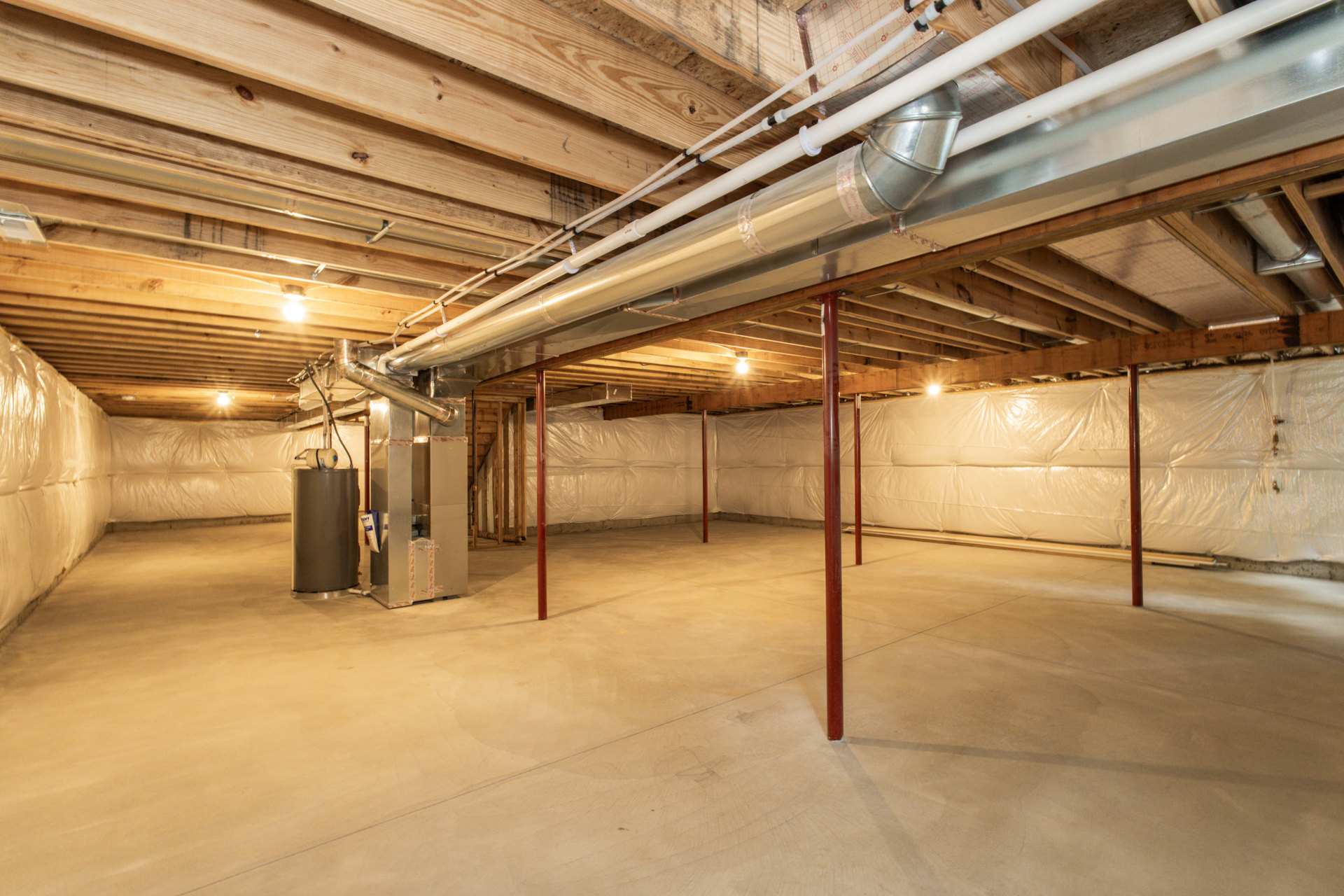 Basement room with exposed ceiling pipes, concrete floor, red support poles, white cylindrical tank, and visible beams.