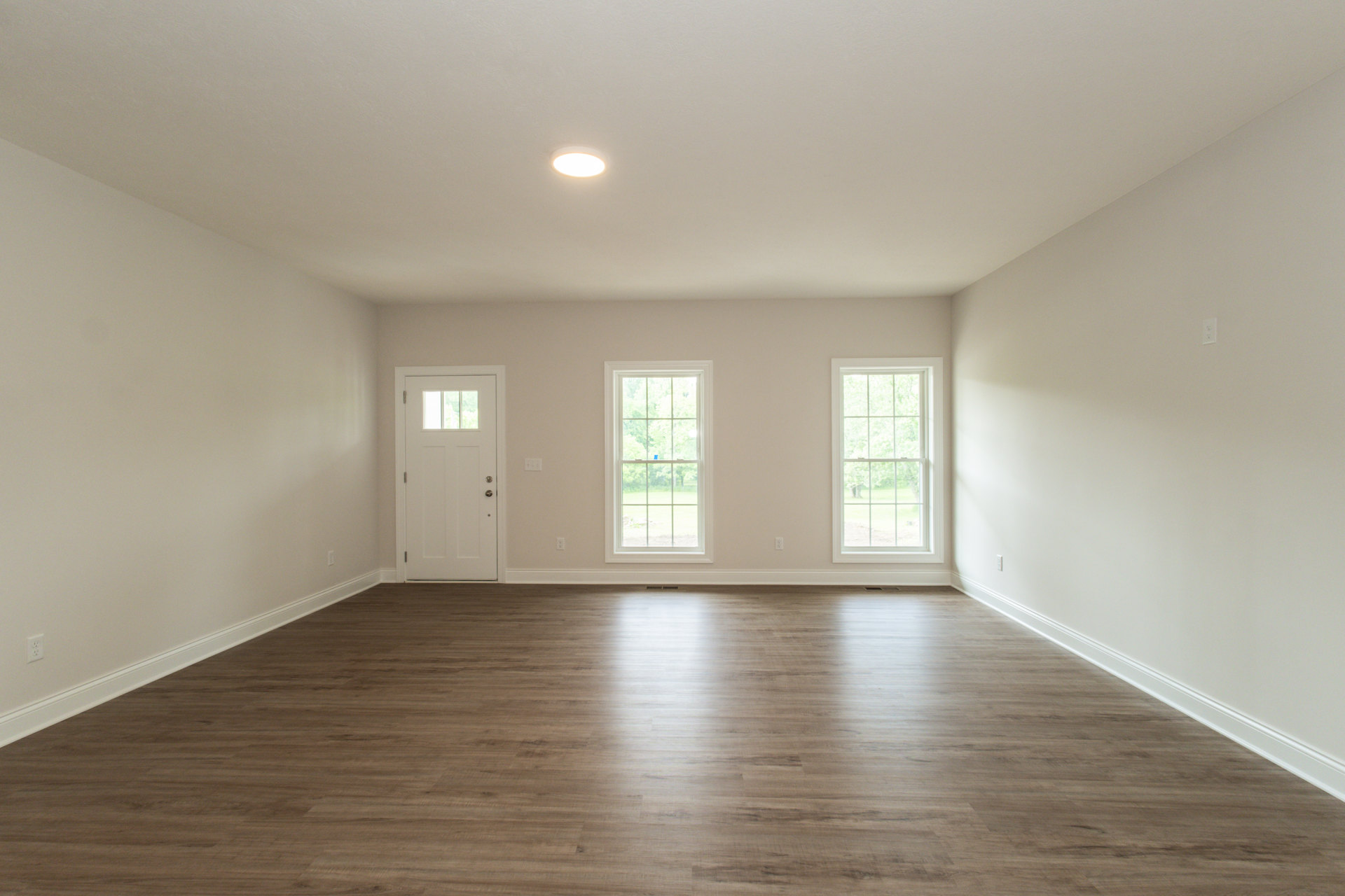 Hardwood floor room with large windows, white door with glass panel, ceiling light fixture, plaster walls, view of trees through windows
