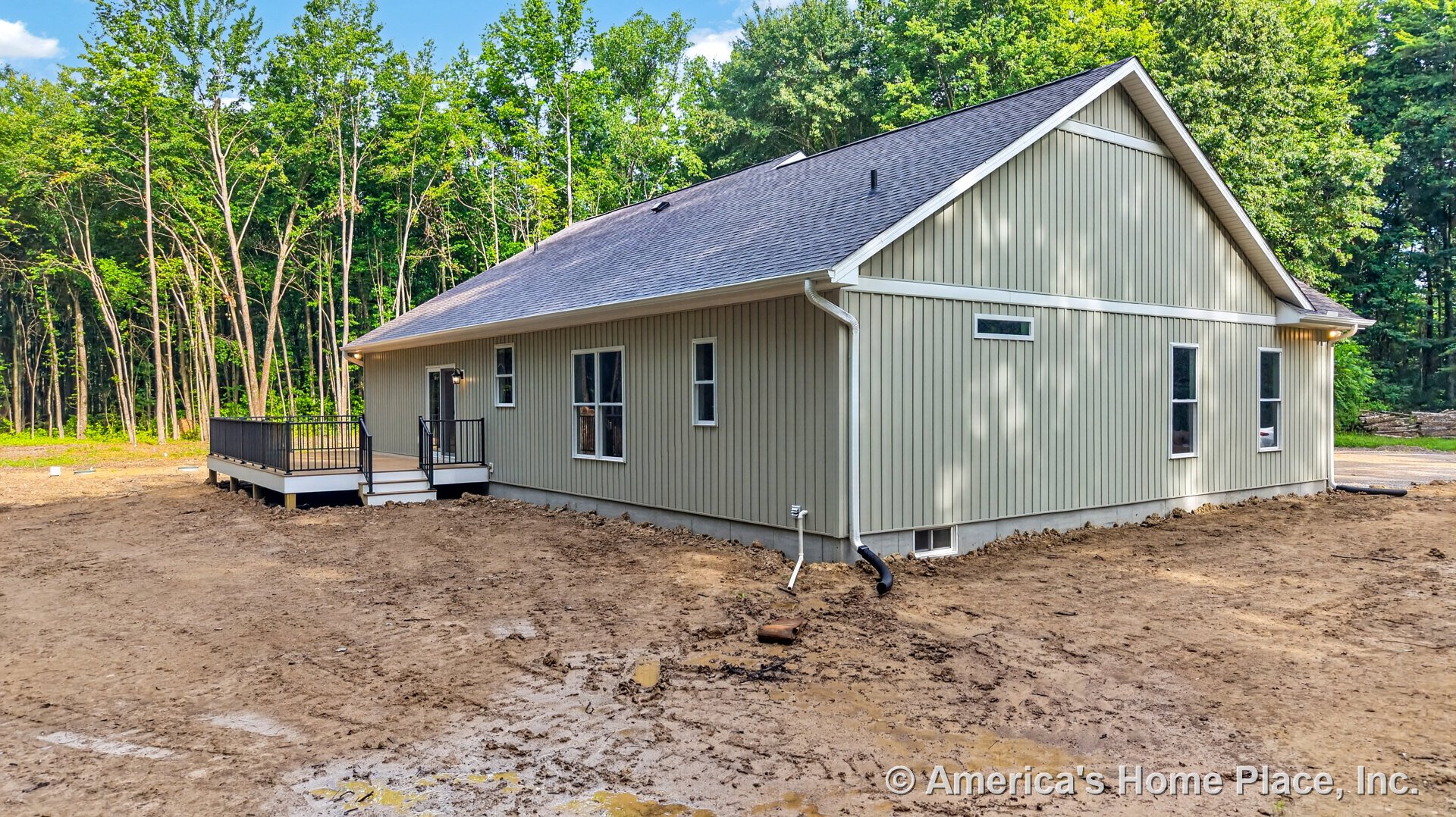 Vertical panel siding exterior with multiple rectangular windows, raised deck featuring black metal railings and stairs, sloped shingle roof, white trim and gutters, outdoor