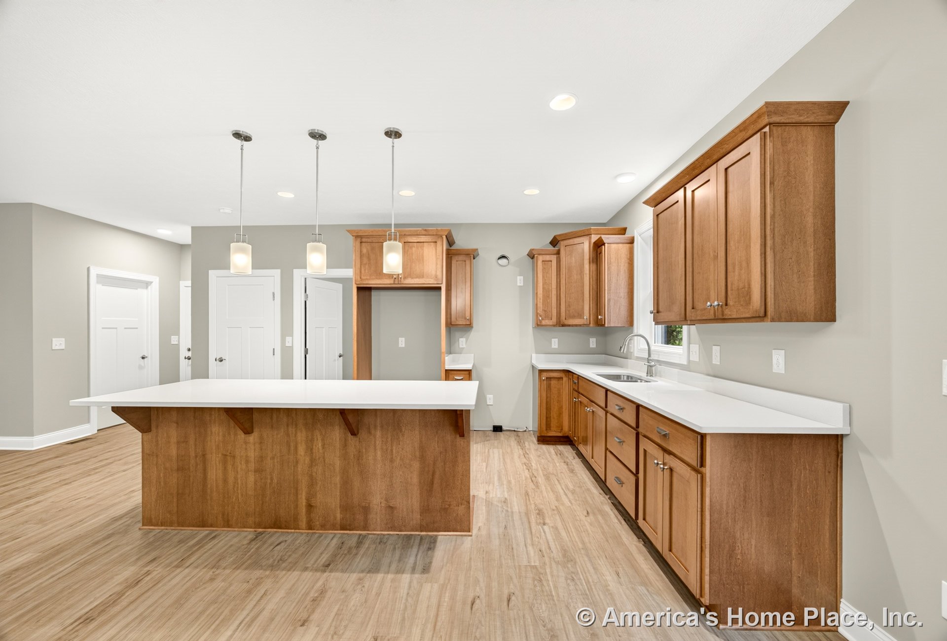 Wood cabinetry kitchen with white quartz countertops, large central island, pendant and recessed ceiling lights, vinyl plank flooring, single bowl sink beneath window, neutral wall