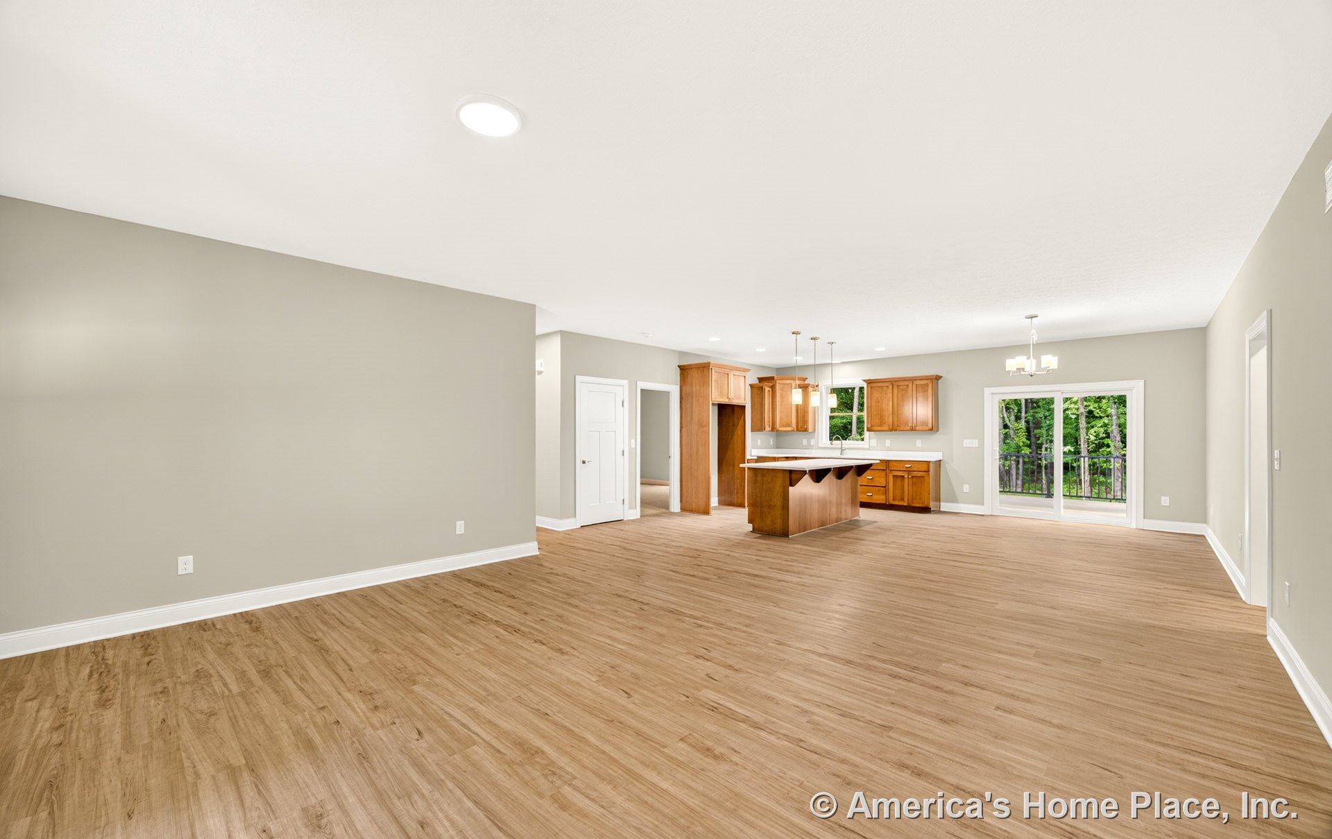 Open-concept kitchen with wood cabinetry, spacious island, recessed and pendant lighting, sliding glass doors to deck, light wood flooring, white trim, and adjacent dining area.
